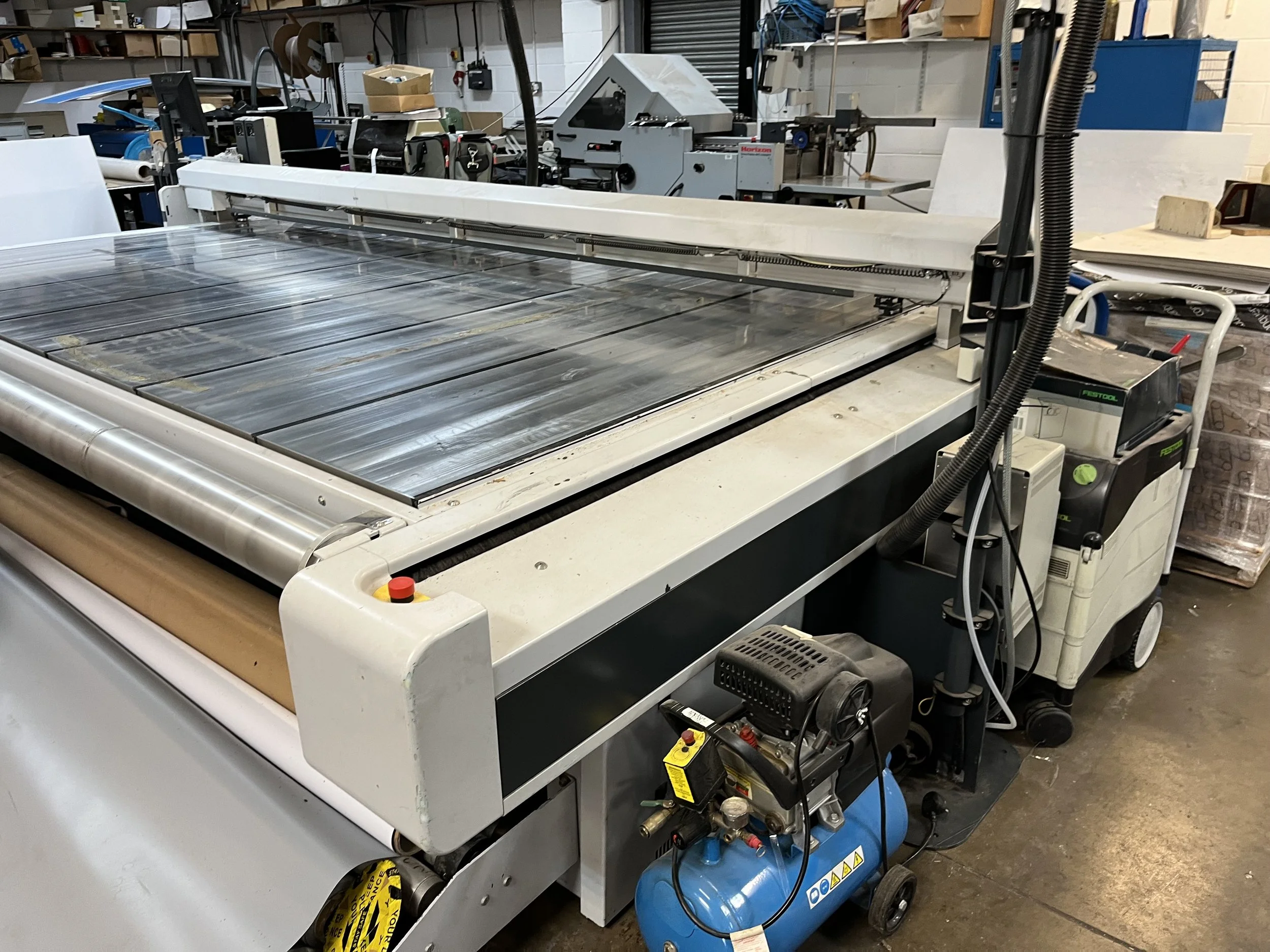 Industrial workshop with a large CNC machine, various tools, parts, and storage shelves in the background.