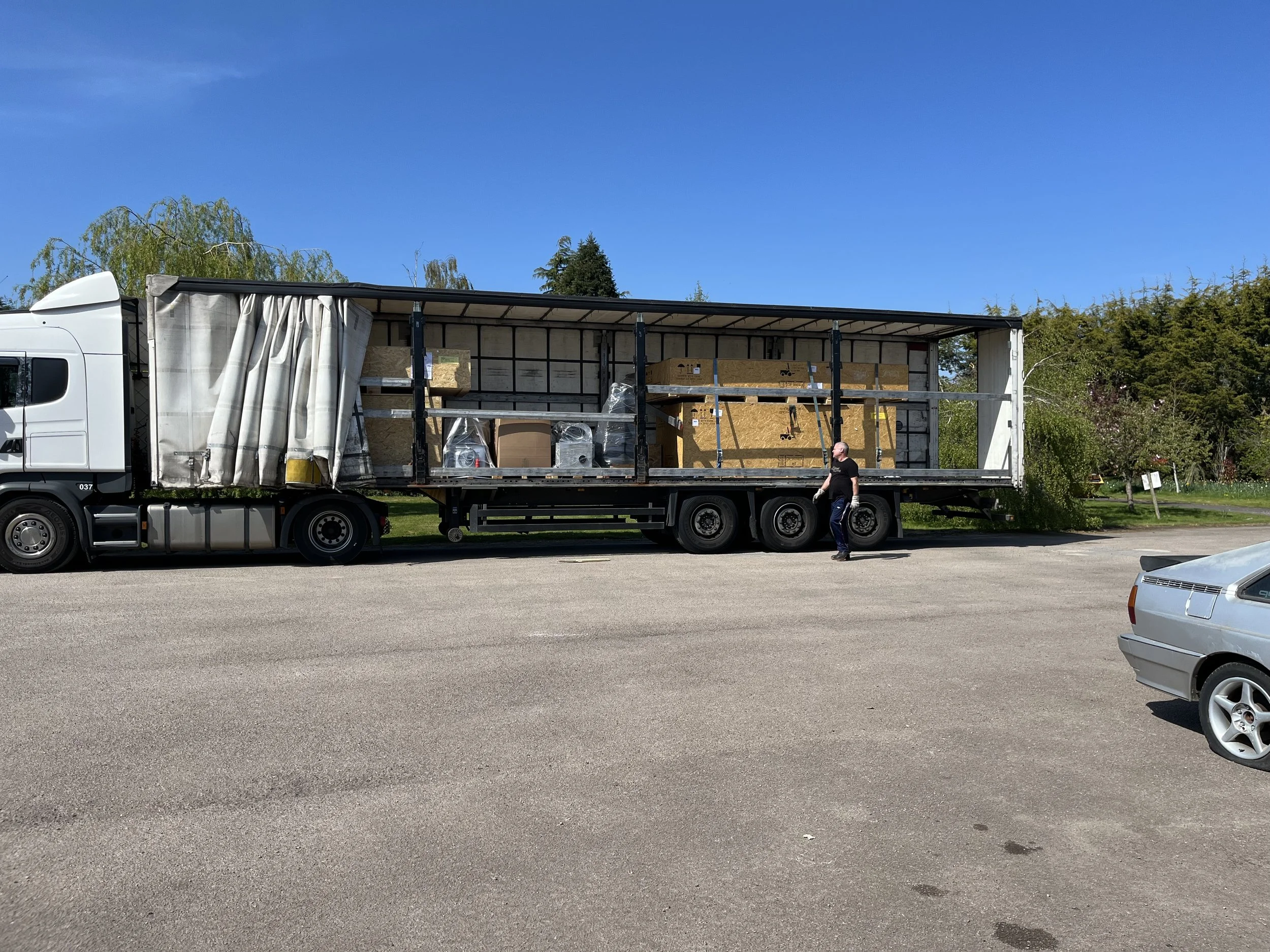 Open moving truck with wrapped and unpackaged furniture and boxes inside, parked on a street with trees and a clear blue sky in the background.