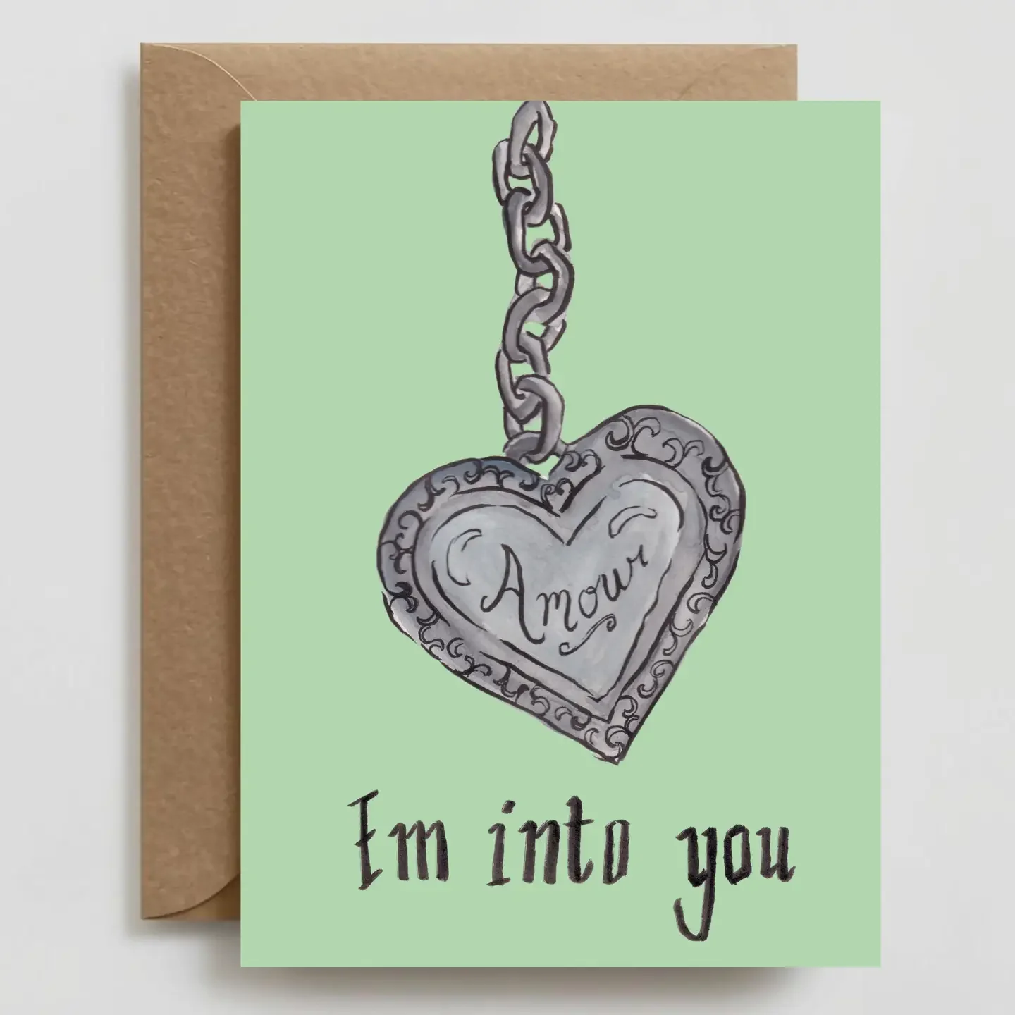 A greeting card with a heart-shaped pendant engraved with the word 'Amour'. The card features a hand-drawn illustration of the pendant and chain on a light green background, with the phrase 'I'm into you' written below.