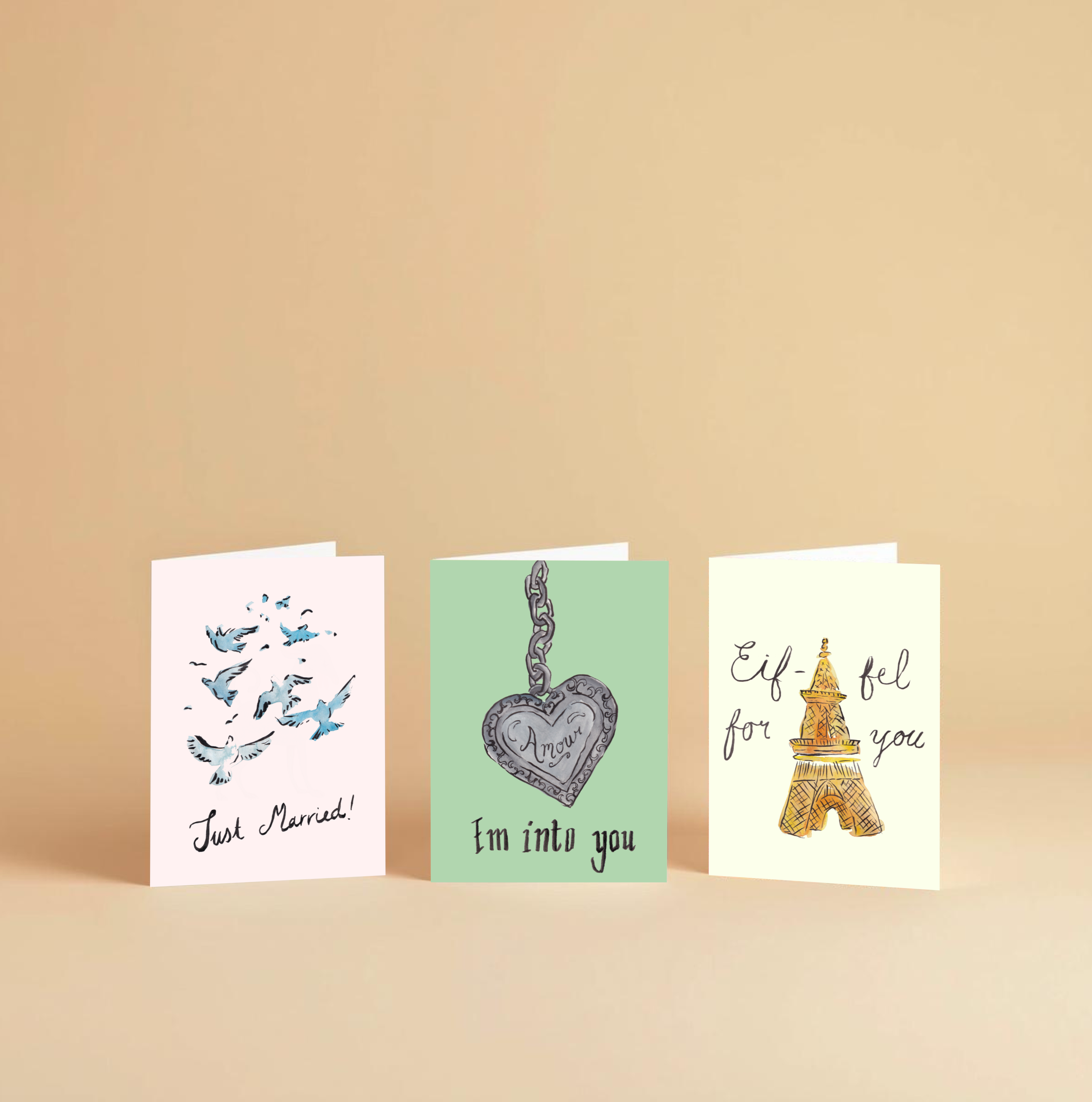 A beige-colored wall with four notes and cards attached at the bottom. The notes contain various messages and illustrations, including a pattern of flying birds, a heart-shaped locket with the word 'Amour,' and the Eiffel Tower with the message 'Eiffel for you.'