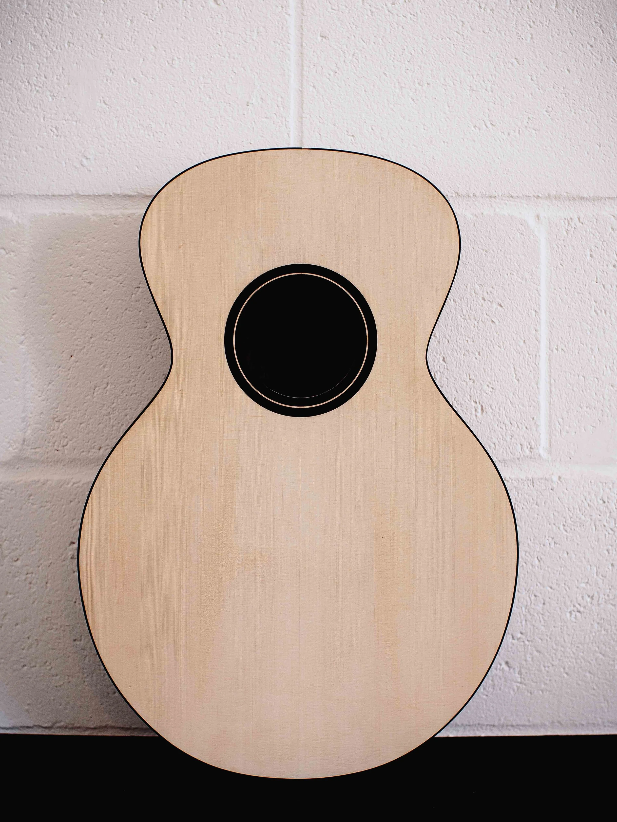 An acoustic guitar, placed against a white brick wall, with shadows cast on a black surface.