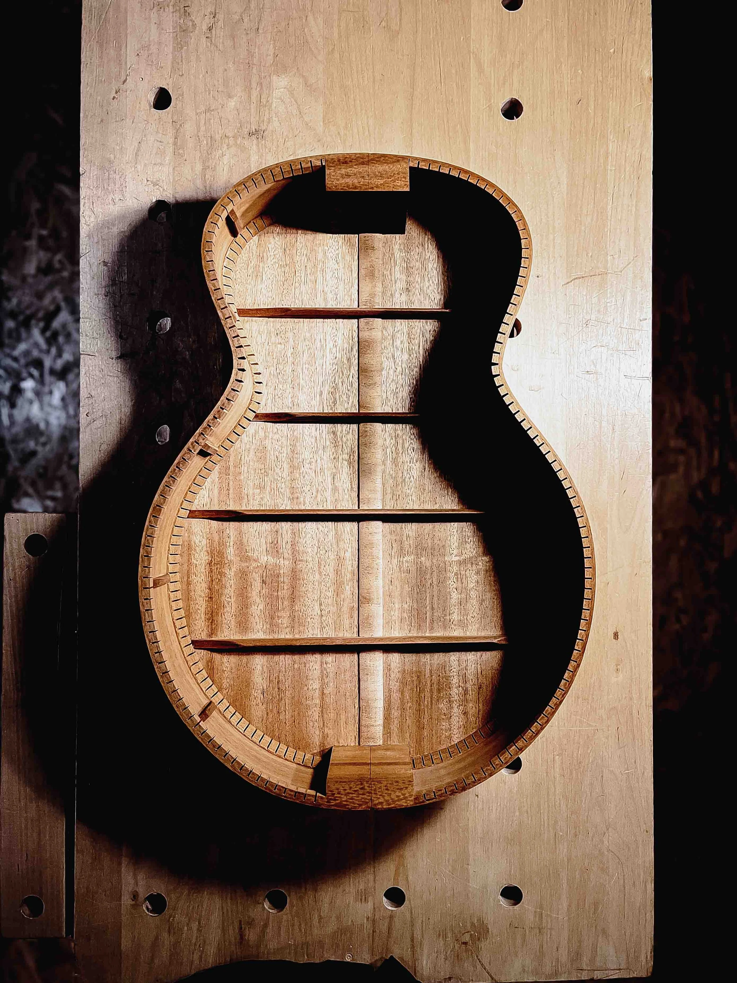 A partially assembled acoustic guitar body, placed on a wooden workbench.