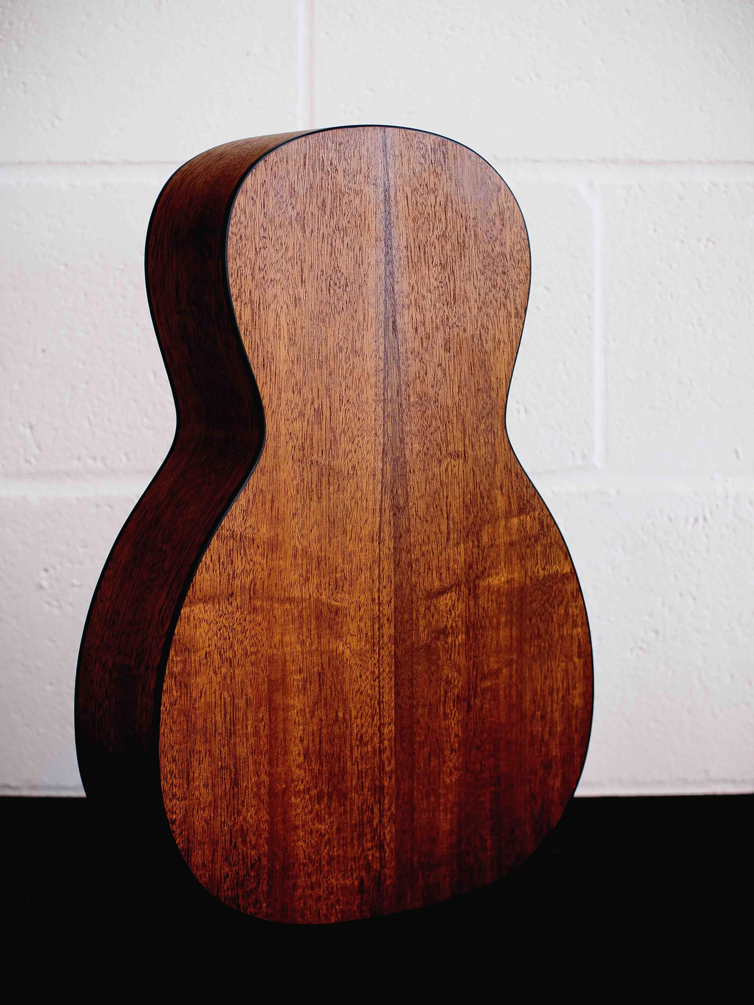 Close-up of the back of a wooden guitar body against a white wall.