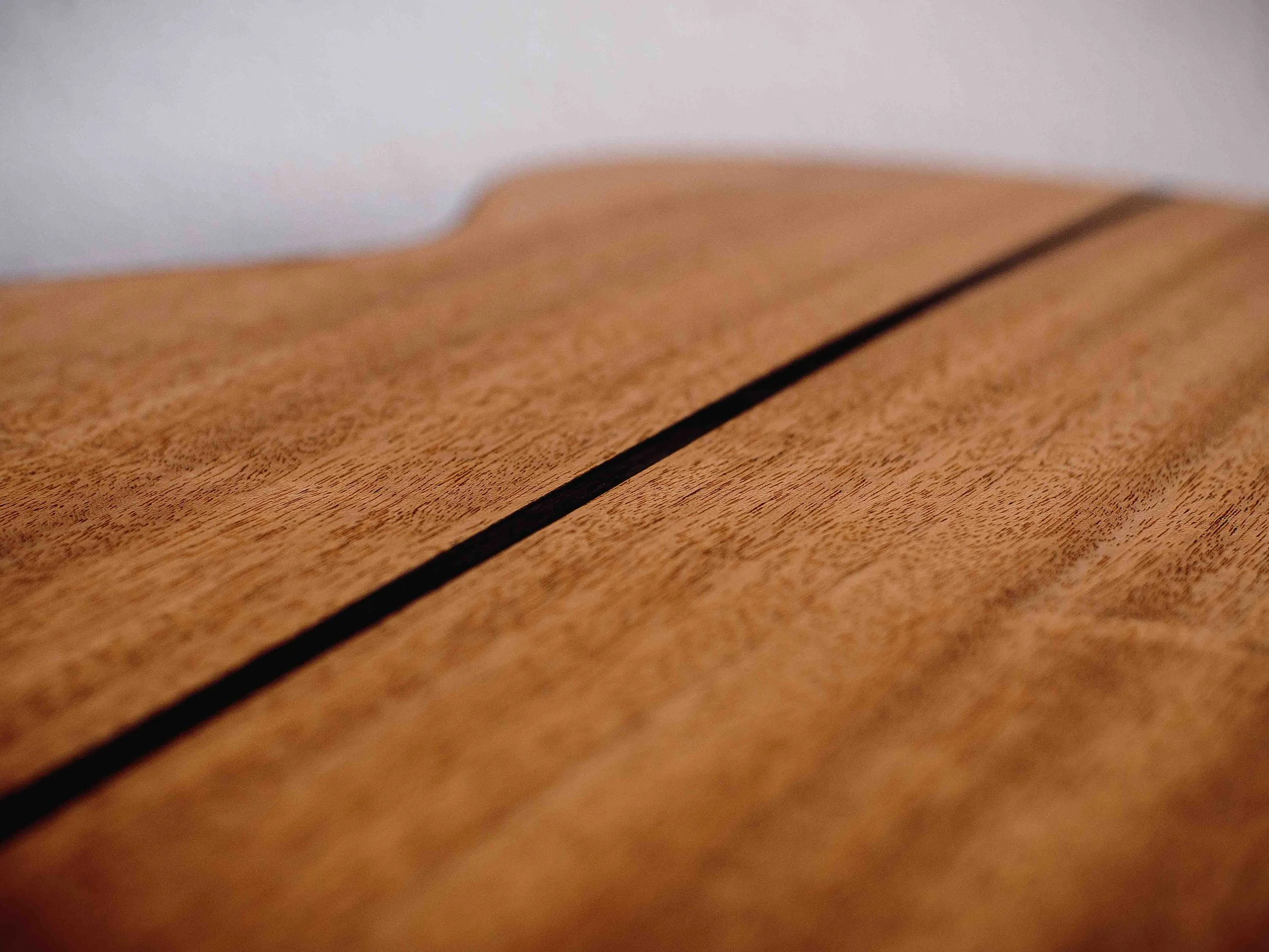 Close-up of the back of an acoustic guitar with a ebony centre line running across it and a white wall in the background.