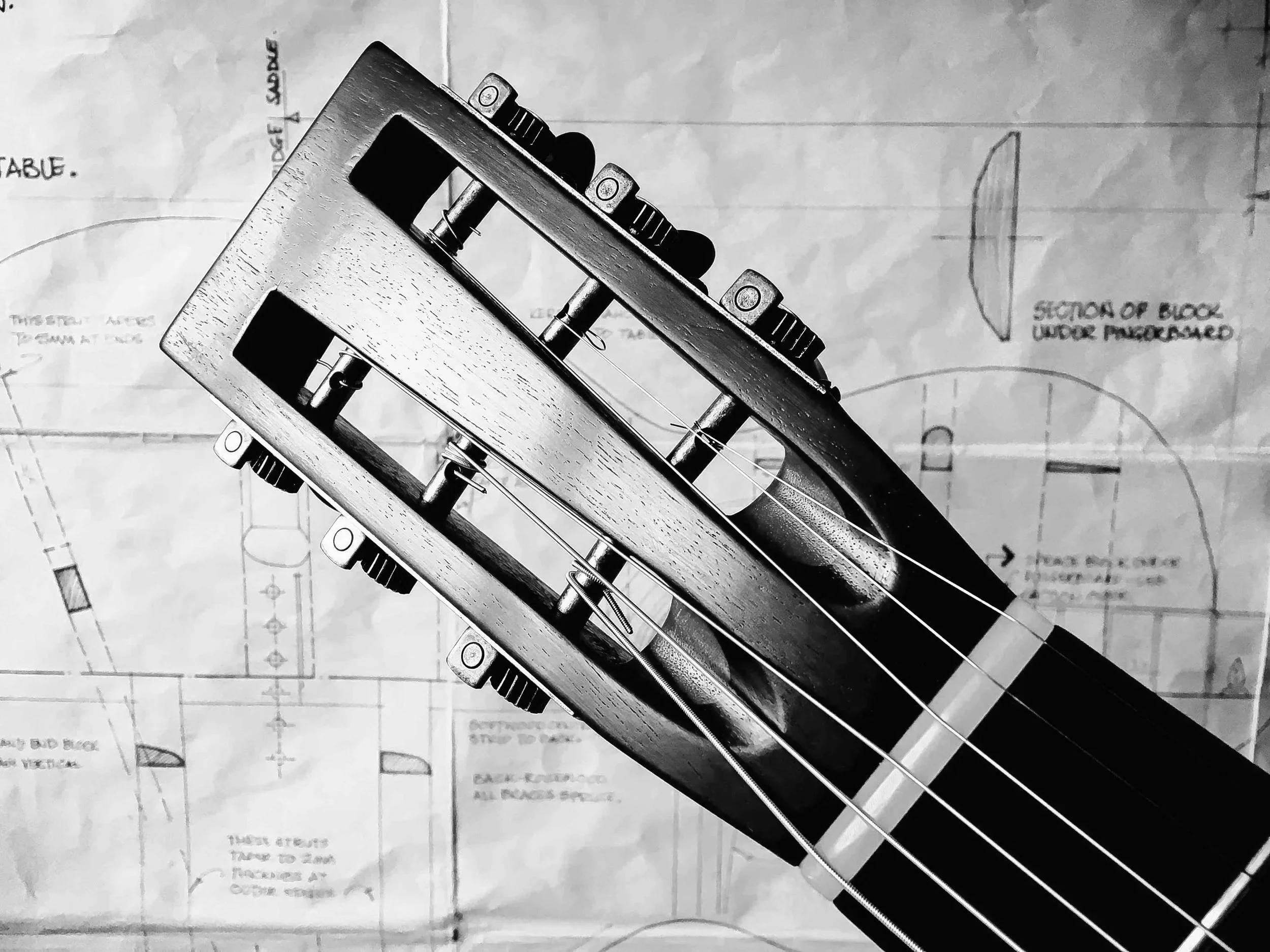 Close-up black and white photograph of a guitar, set against background of engineering or architectural drawings.