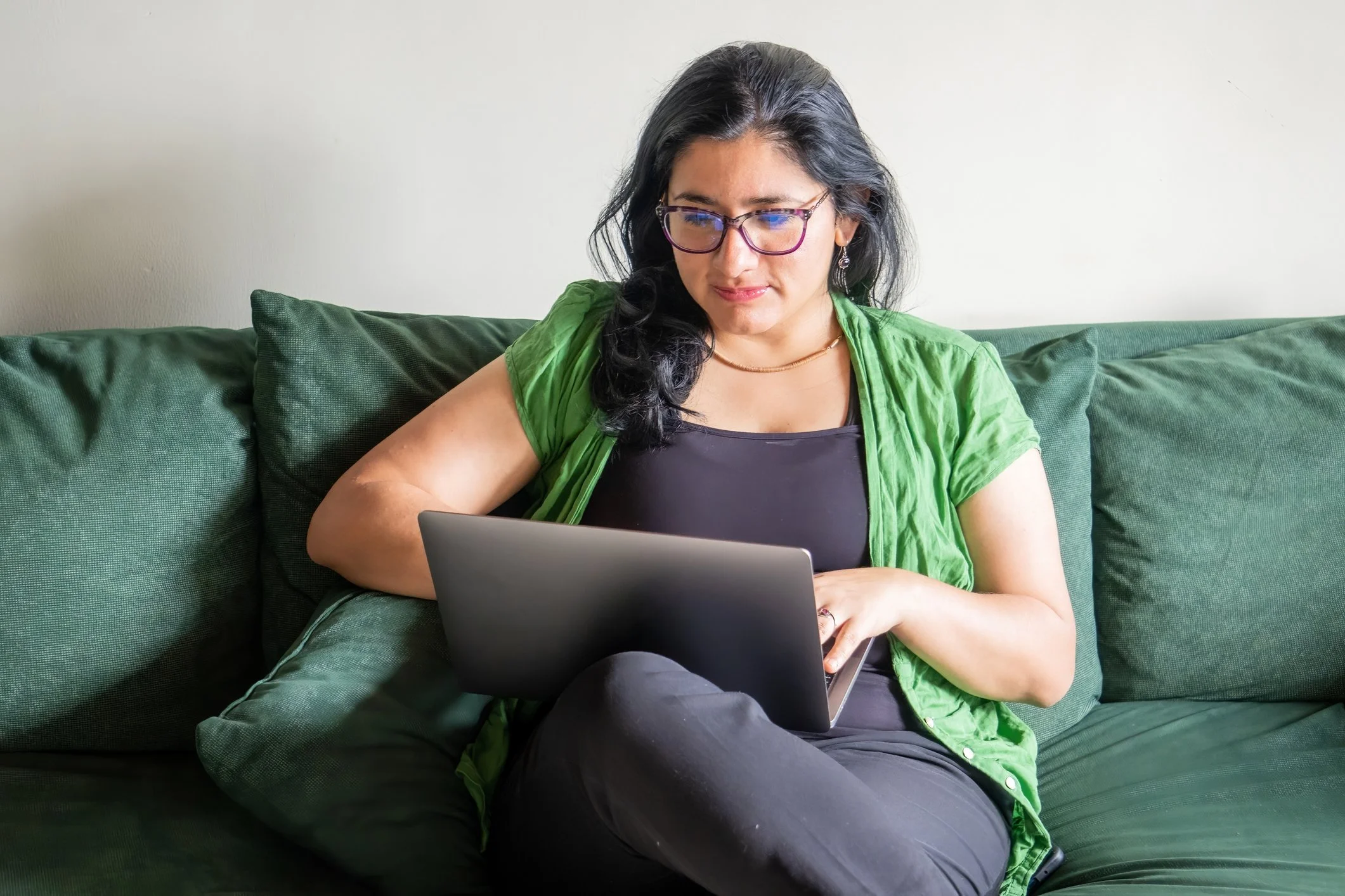 A Chime Housing customer is sitting in their living room on a green sofa using their laptop