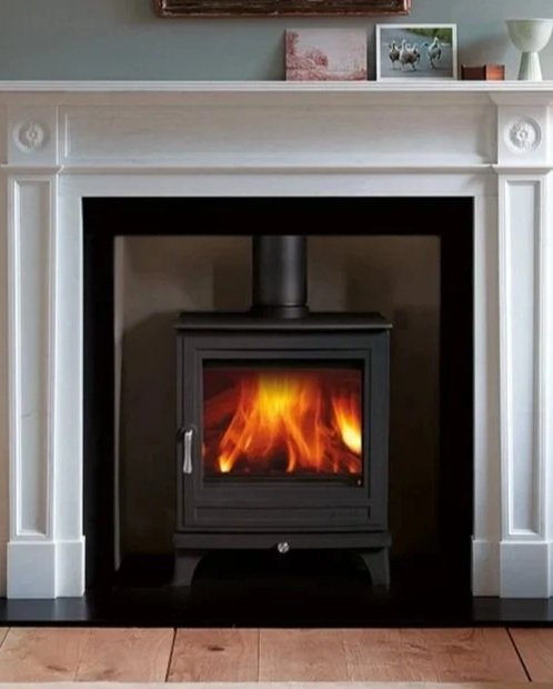 A black wood-burning stove inside a fireplace with a white mantel, showing a fire burning inside the stove.
