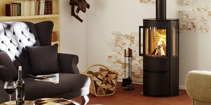 Living room with a black fireplace, a dark gray tufted armchair, a bookcase, a wine glass, a bottle of wine, and a basket of firewood.