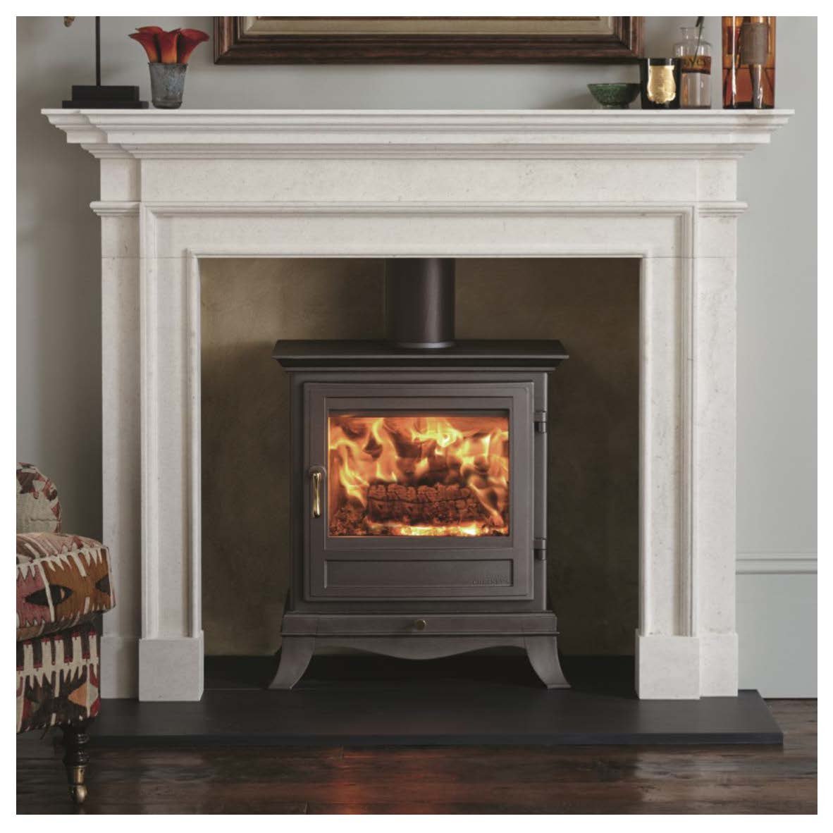 A fireplace with a white mantel and a black wood stove with a fire burning inside, set on a dark hardwood floor.