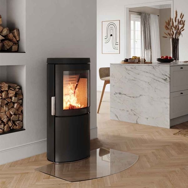 Modern living room with a black pellet stove, fire burning inside, wood logs stored in built-in shelves, and a marble kitchen island in the background.