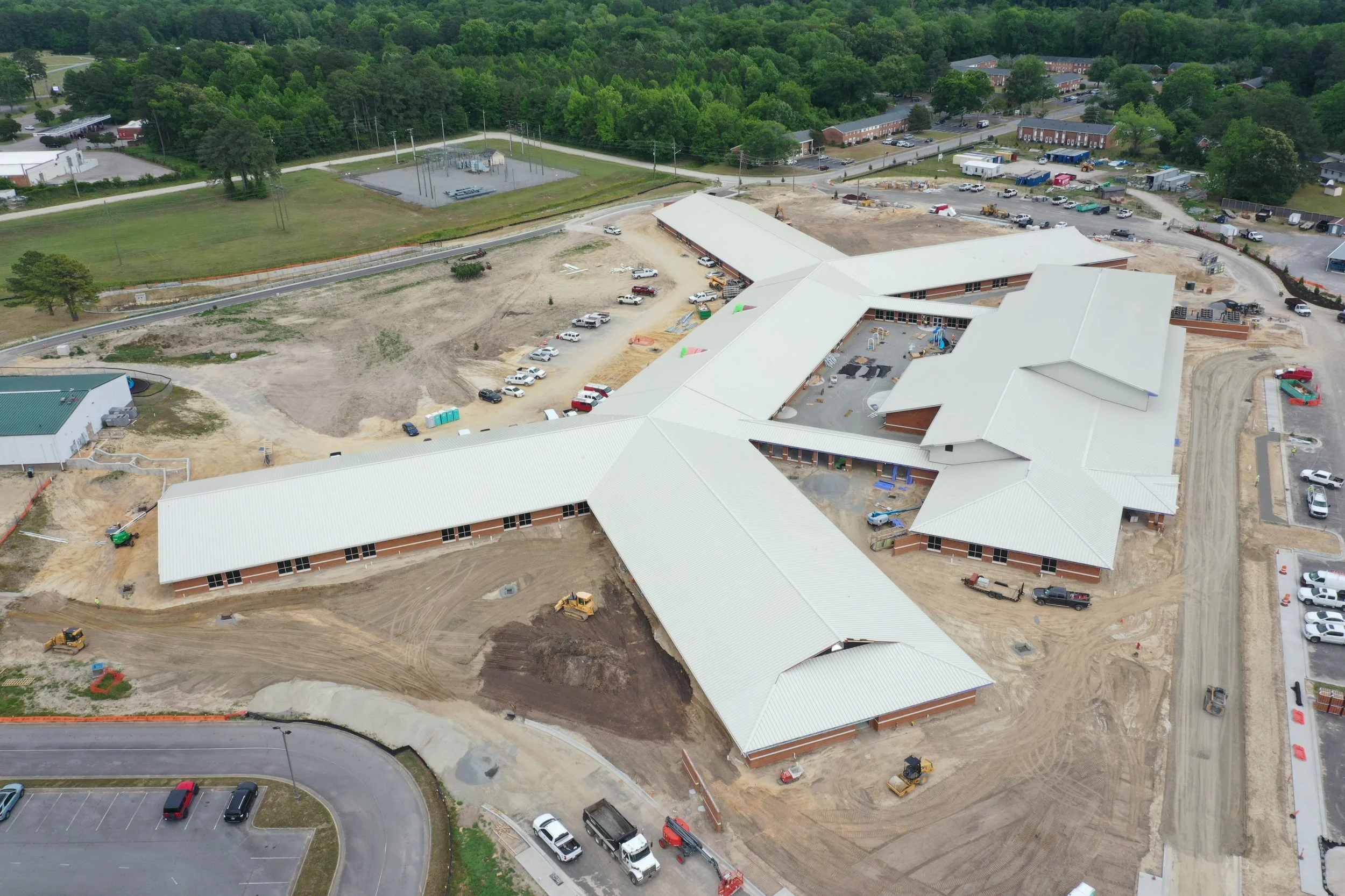Aerial view of a construction site with buildings under construction, vehicles, and surrounding green landscape.