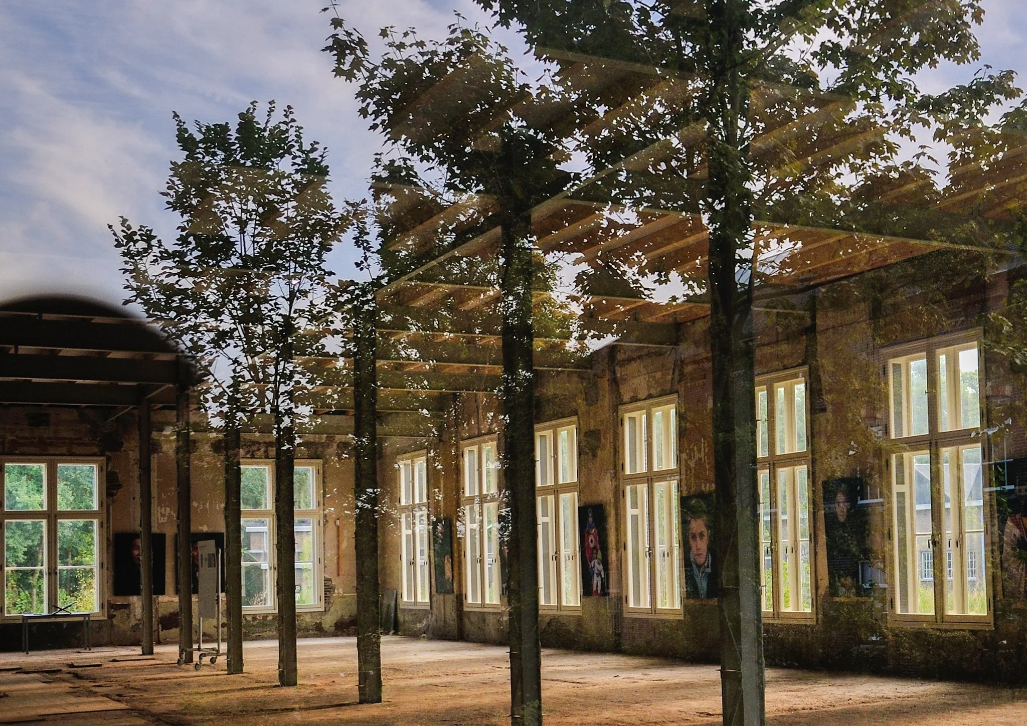 View through a glass window showing an interior under construction with multiple large windows, wood beams, and trees outside.