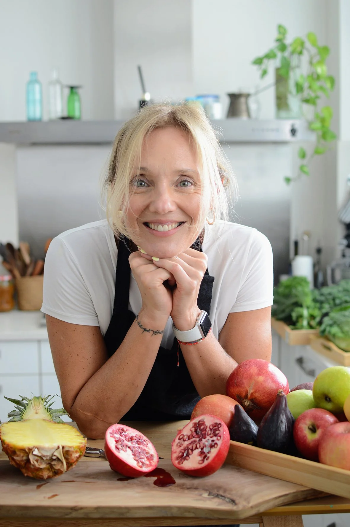 Pepa Poduje en su cocina rodeada de frutas, incluyendo granadas, piña, y manzanas.