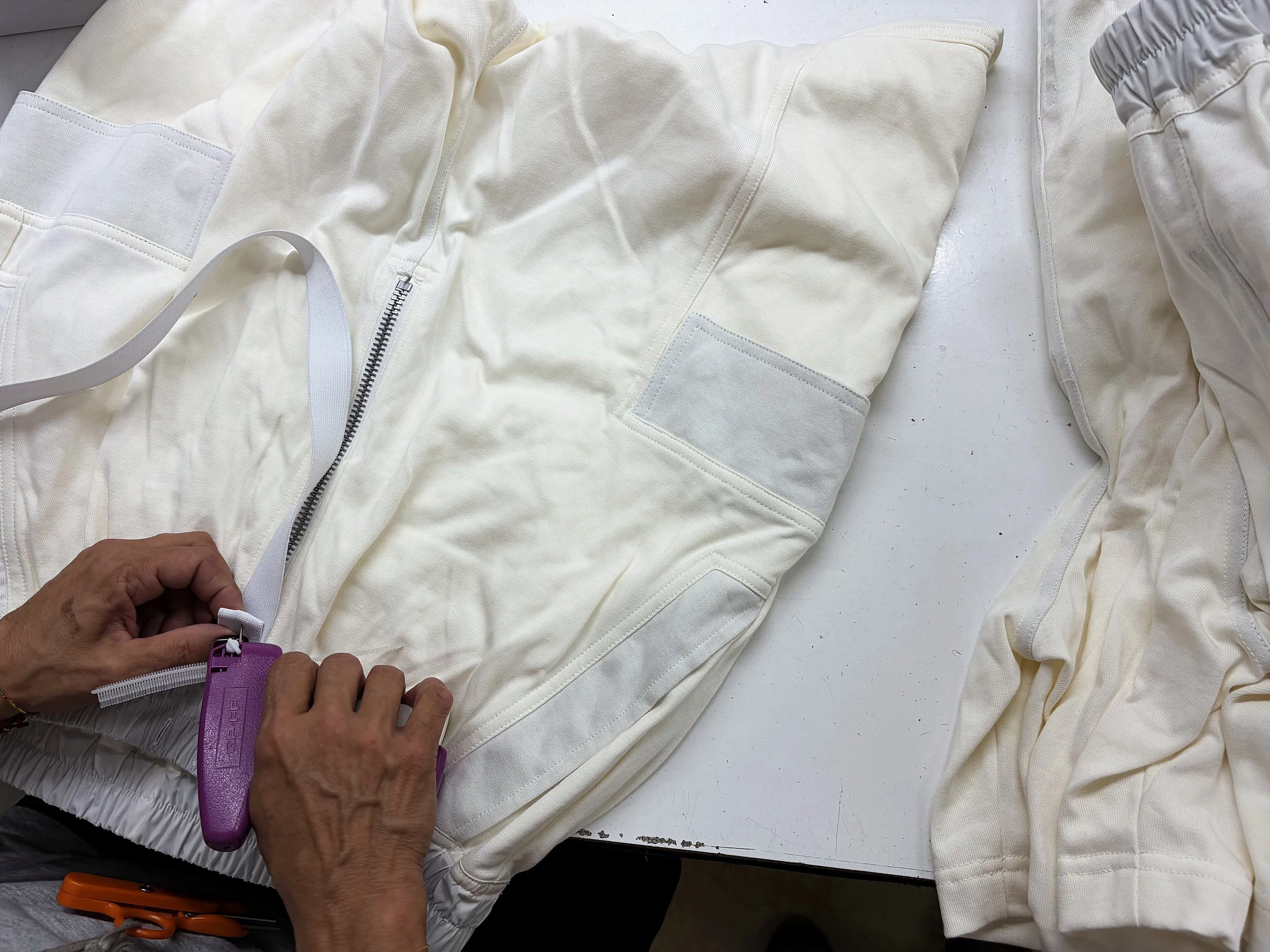 Operaio cuce una giacca tecnica bianca con cerniera e tasche su un tavolo da lavoro di Lineare51, servizi per l'abbigliamento e confezione Rovigo.