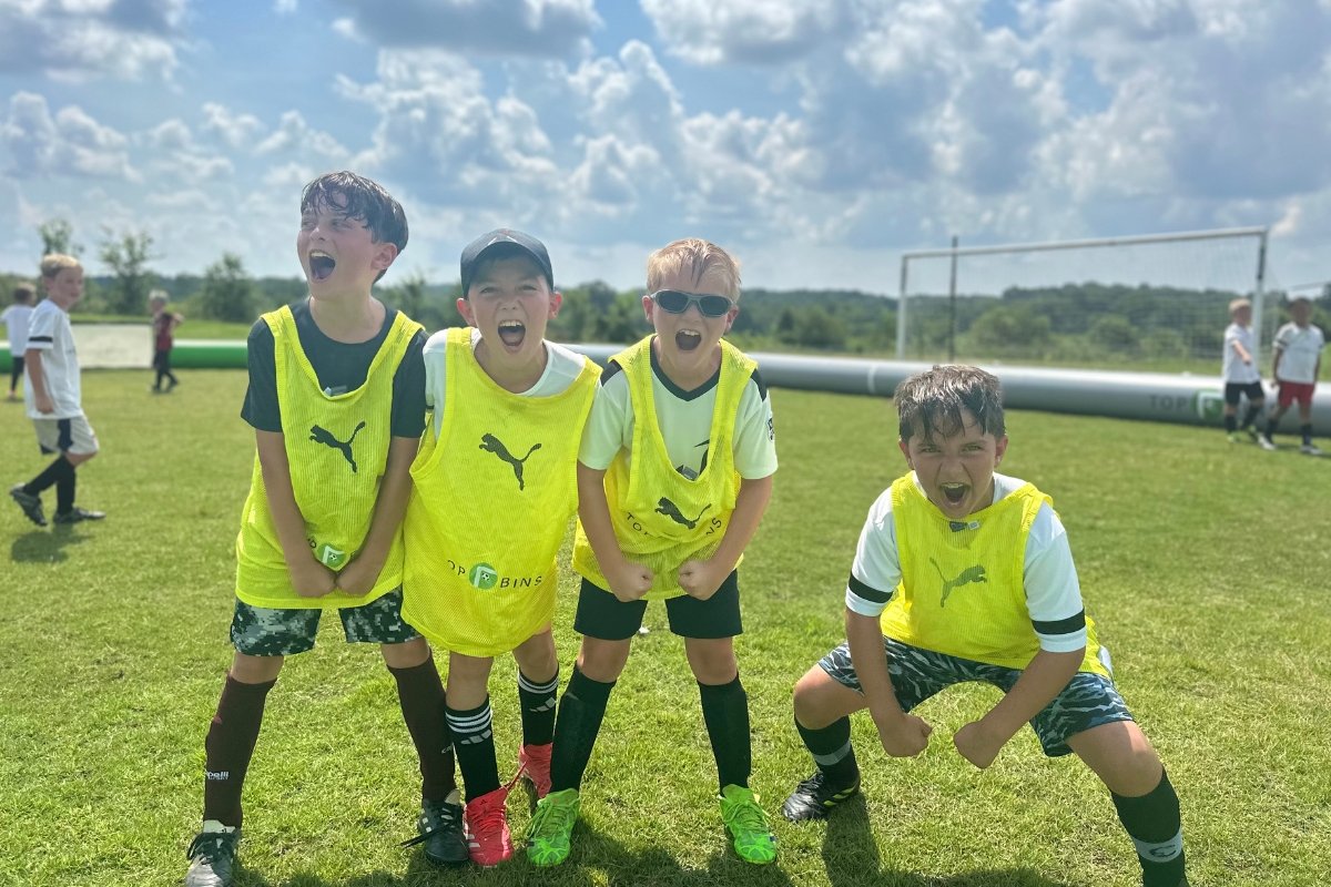 Four boys in soccer uniforms cheering on a soccer field