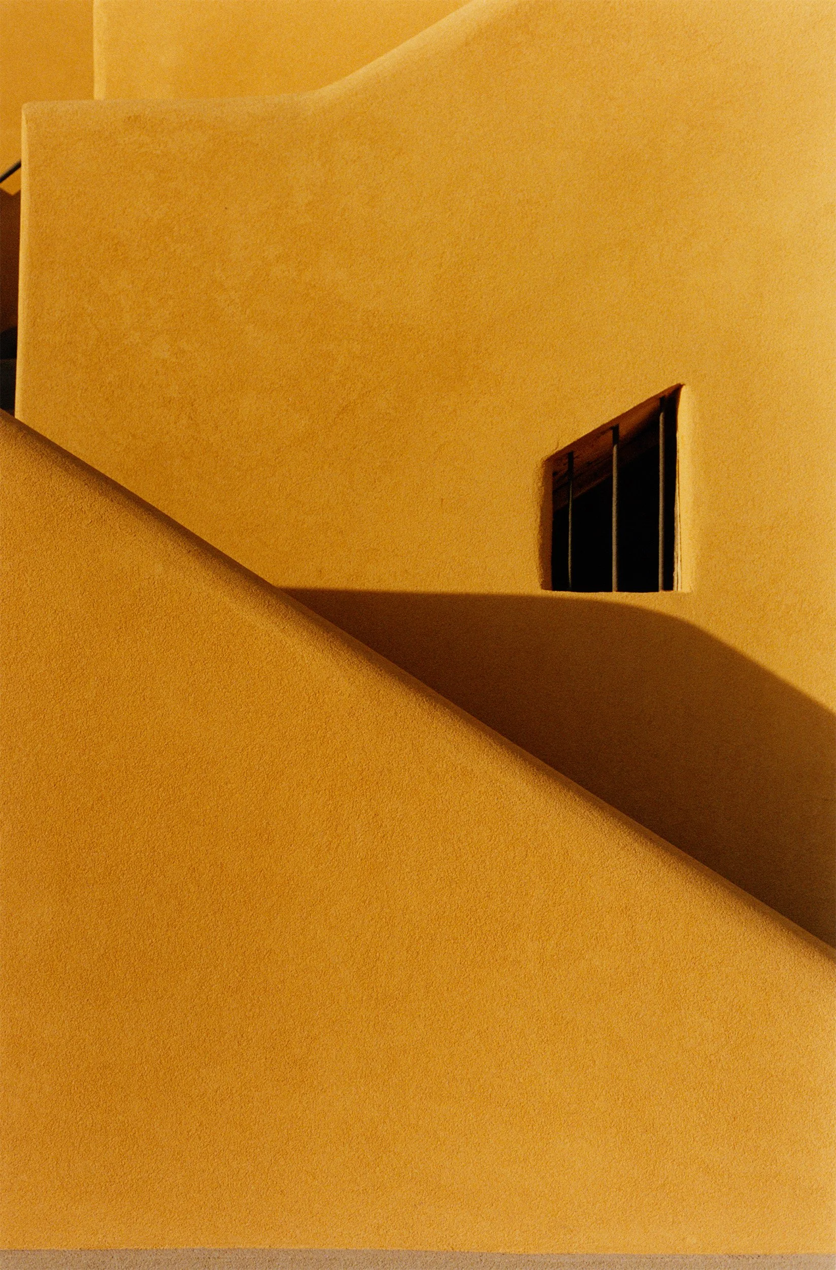 Vue d'une façade jaune d'un bâtiment avec une fenêtre barrée de barreaux noirs.
