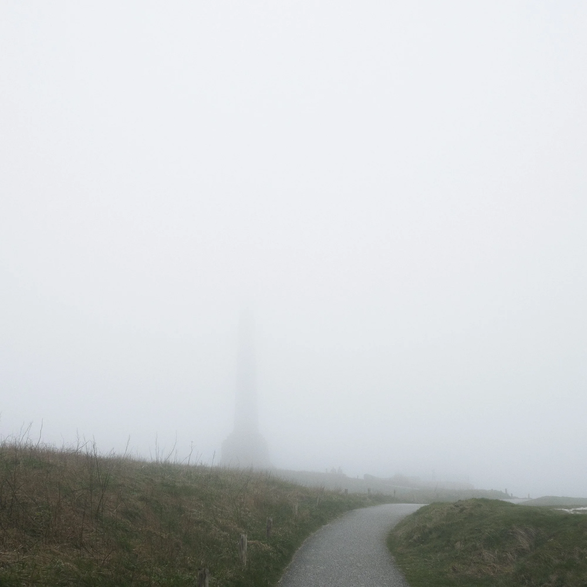 Chemin sinueux bordé de végétation sous un ciel brumeux, paysage rural