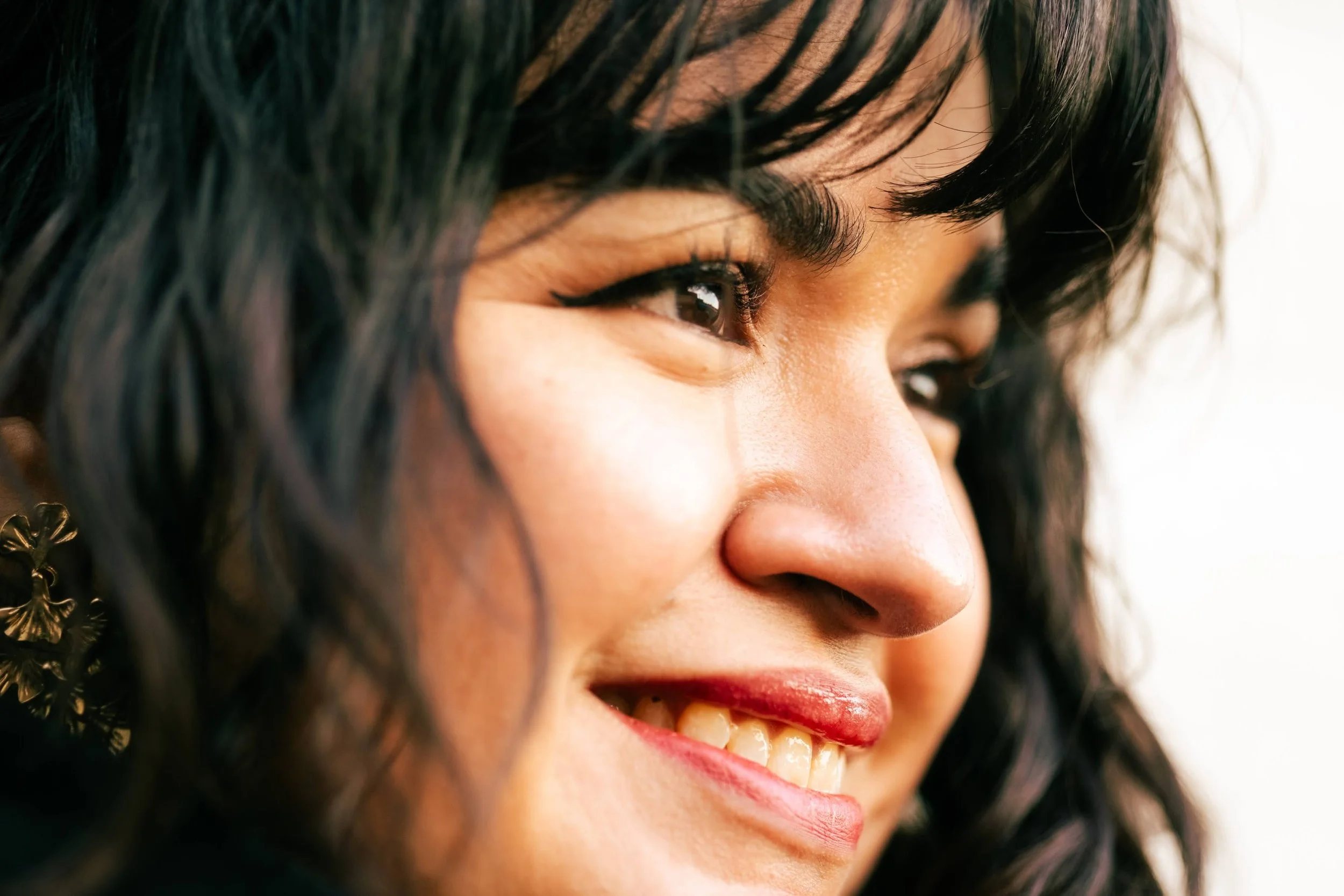 Close-up of a woman smiling, showing her teeth, with dark hair and earrings.
