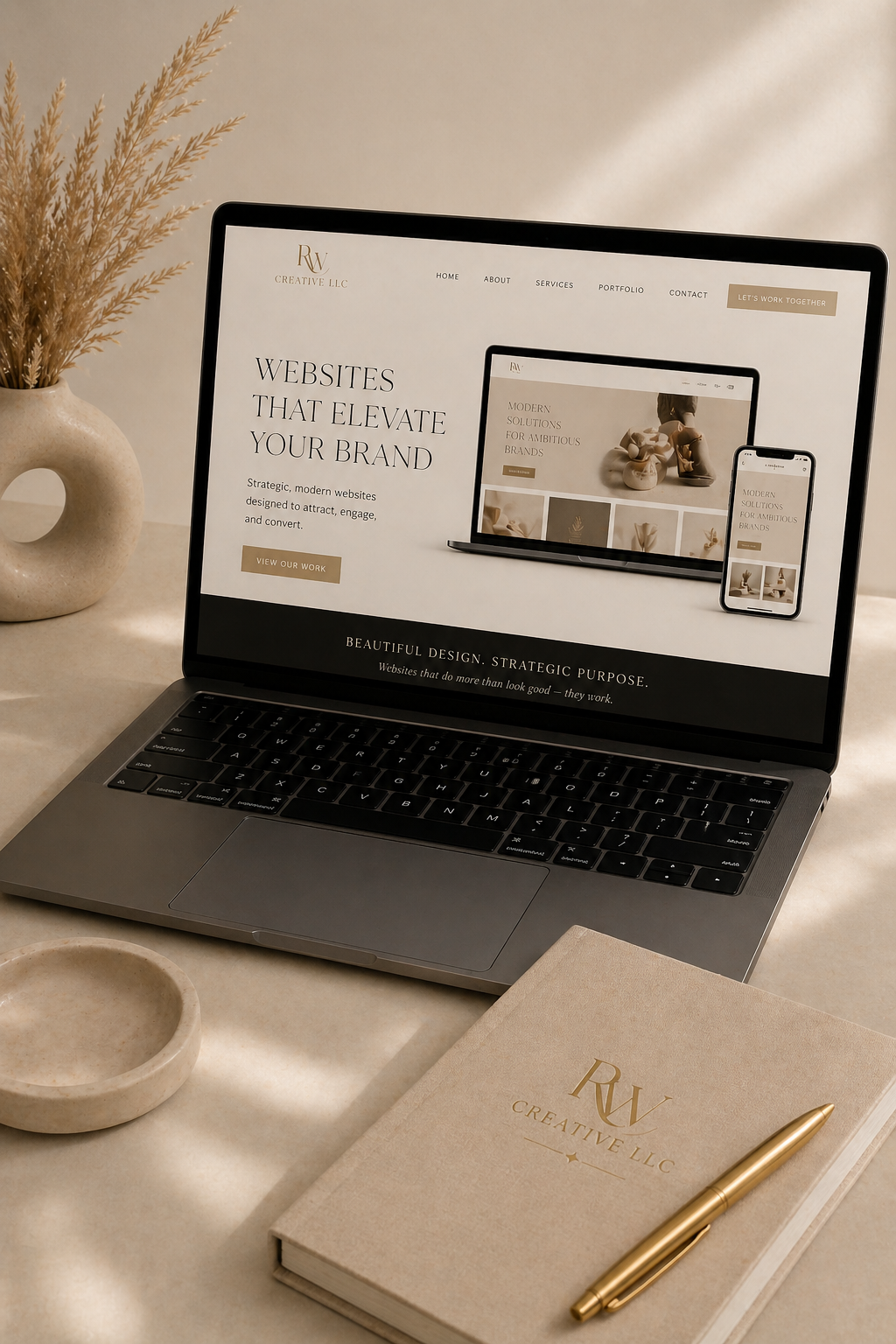 Laptop displaying a website for a creative LLC company, with a notebook, pen, and a decorative vase with dried plants on a beige table.