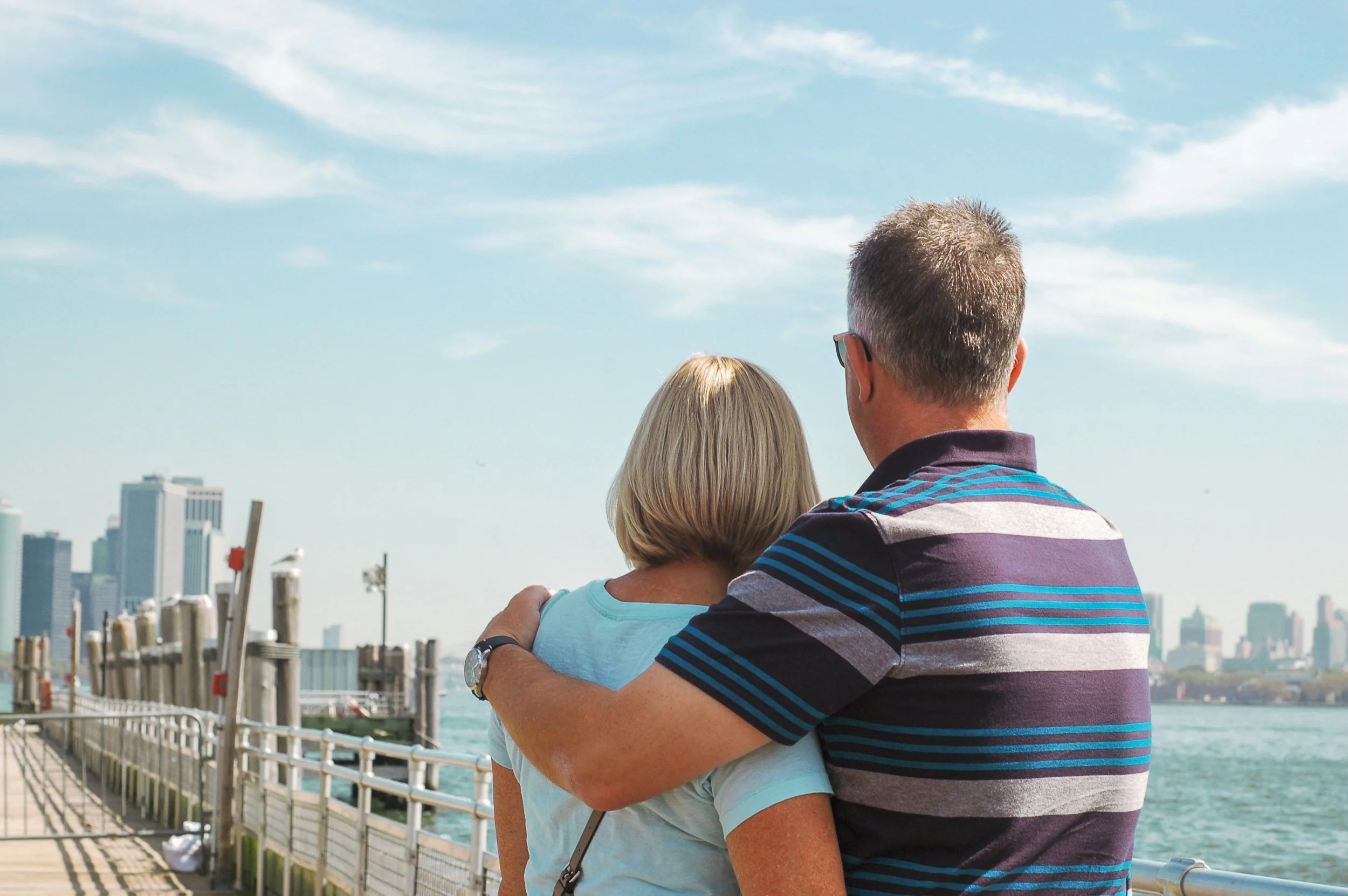 A man and woman standing close together overlooking a city skyline, with the man embracing the woman.