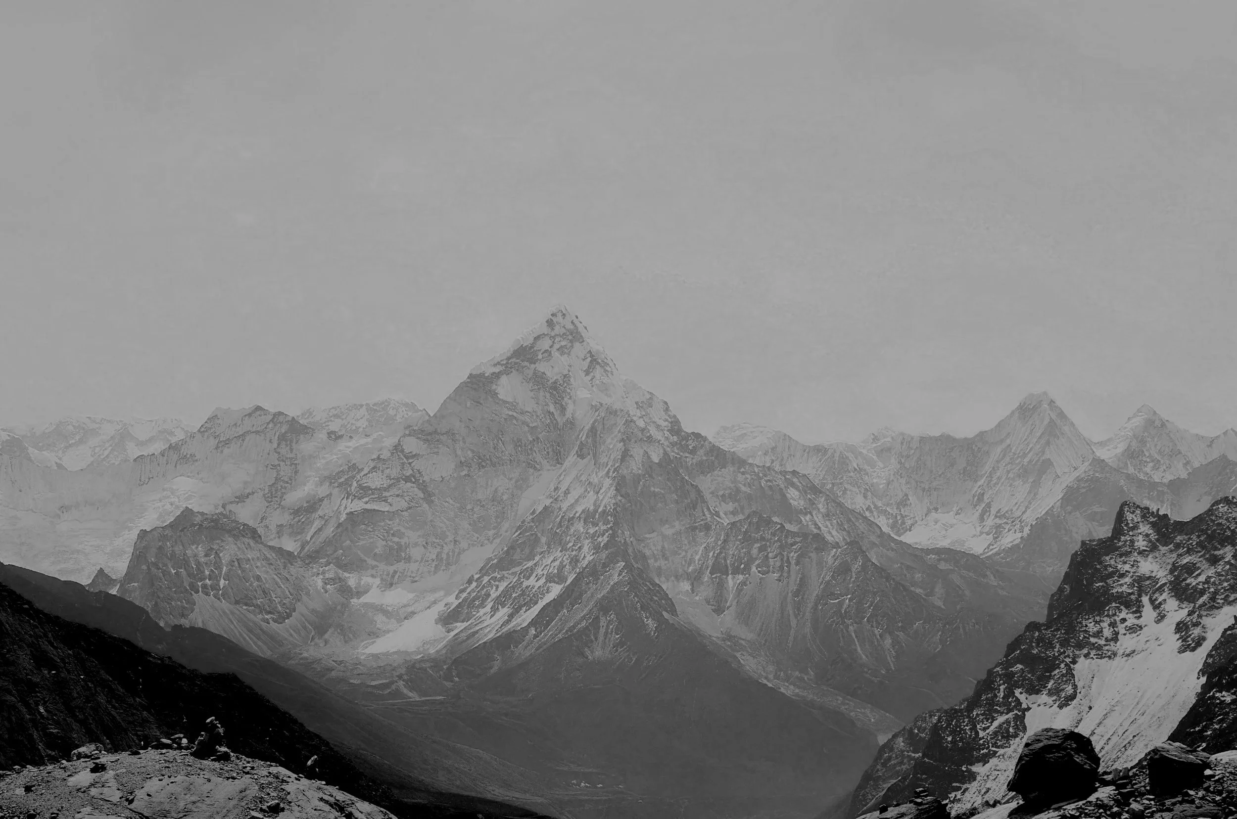 Black and white photograph of a mountain range with snow-capped peaks and a valley below.
