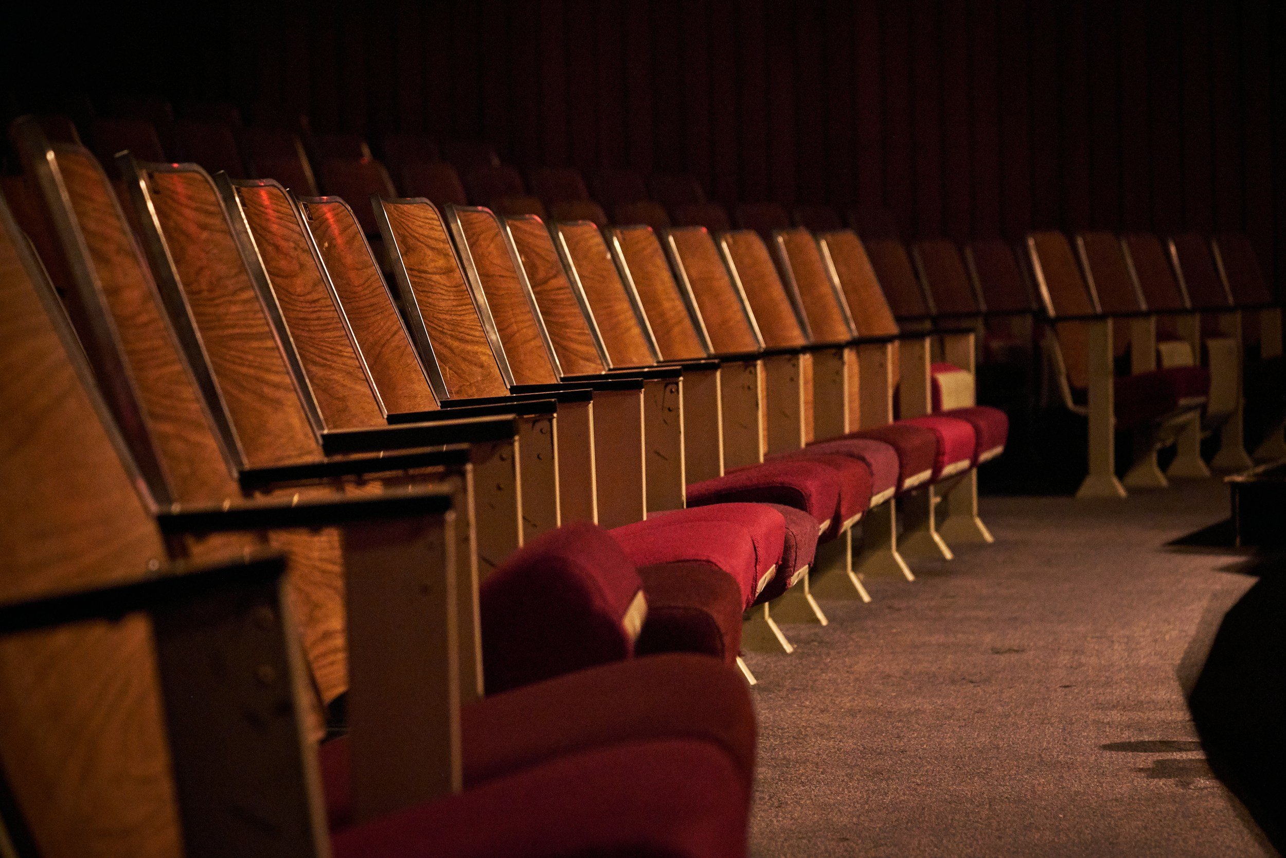 Empty theater with wooden seats and red cushions, dim lighting.