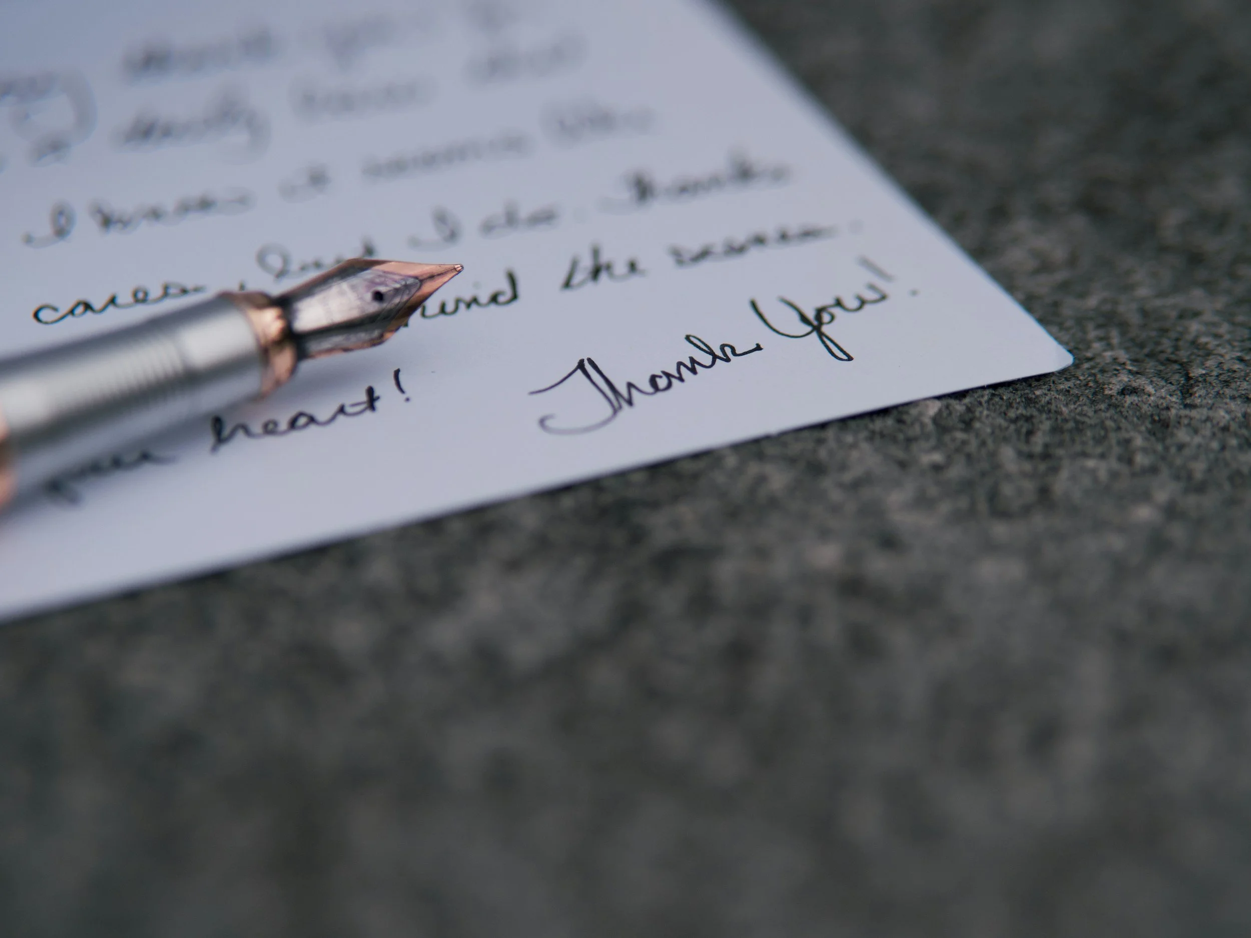 Close-up of a handwritten letter on a piece of paper with a fountain pen resting on top, placed on a textured surface.