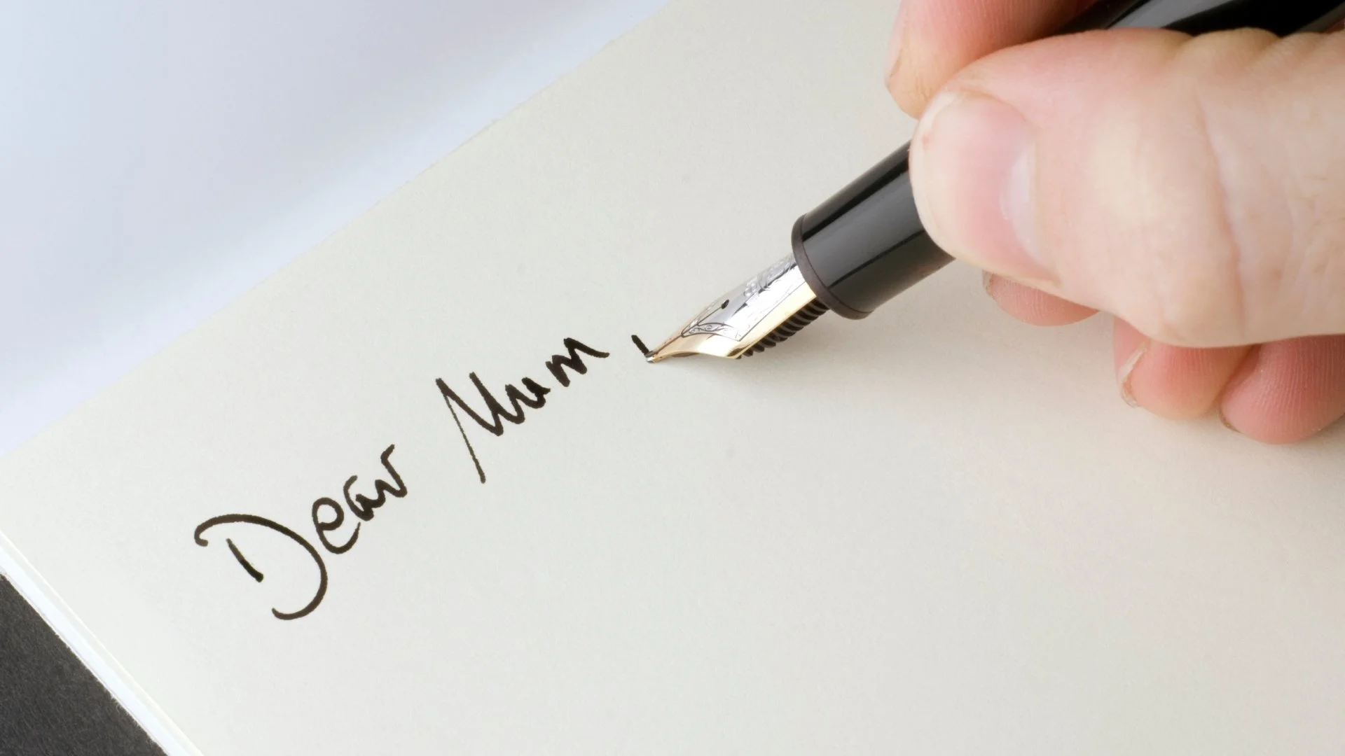 Hand writing "Dear Mom" with a fountain pen on a white piece of paper.