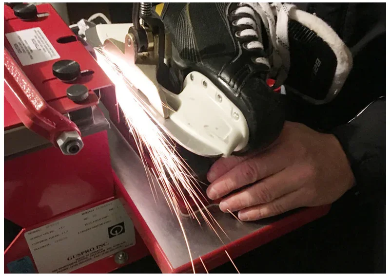 A person sharpening a hockey skate with a grinding machine, sparks flying from the blade.