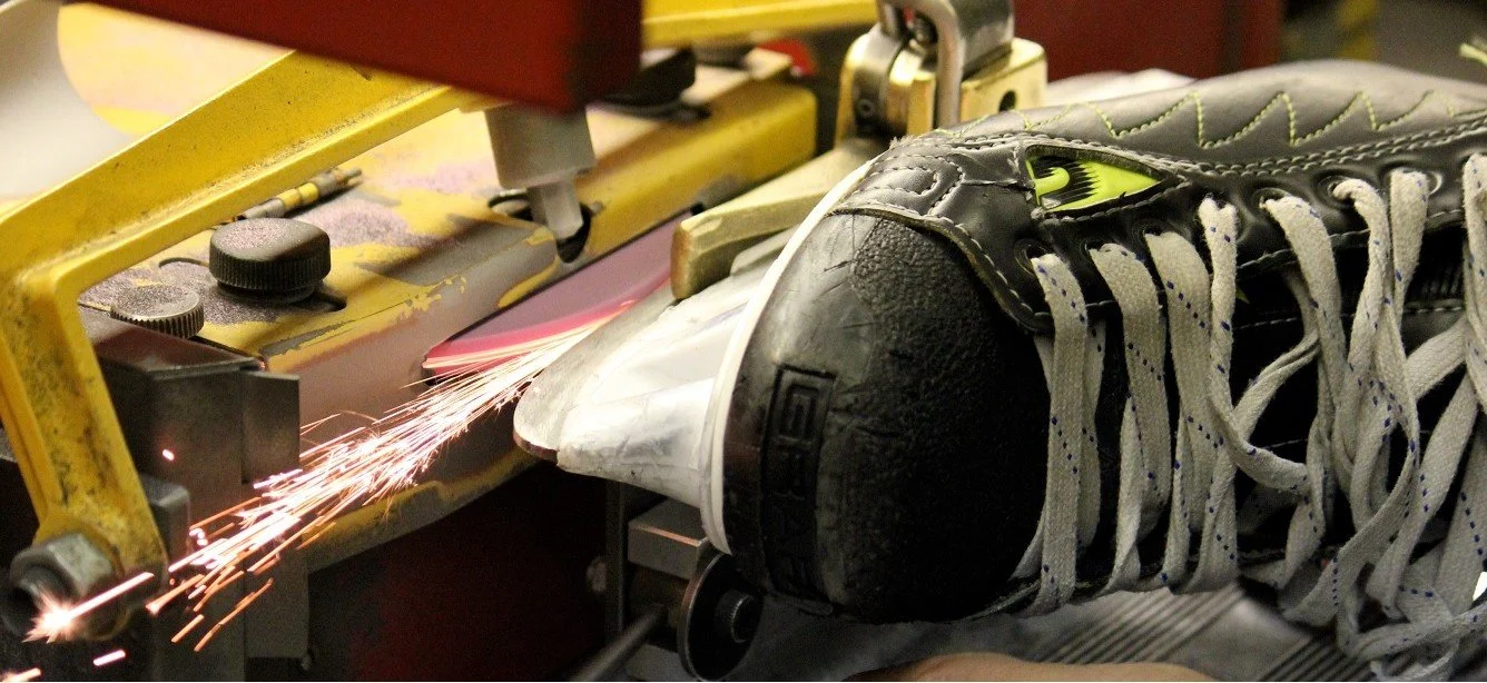 A hockey skate being sharpened on a sharpening manchine with sparks flying.