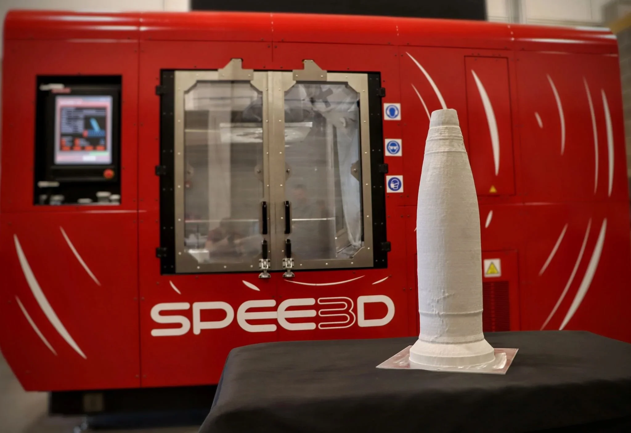 A 3D printer with the branding 'Speed3D' on a red enclosure printing a cone-shaped object on a black surface.