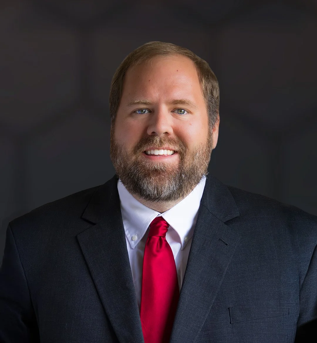 A man with a beard in a business suit and red tie smiling at the camera.