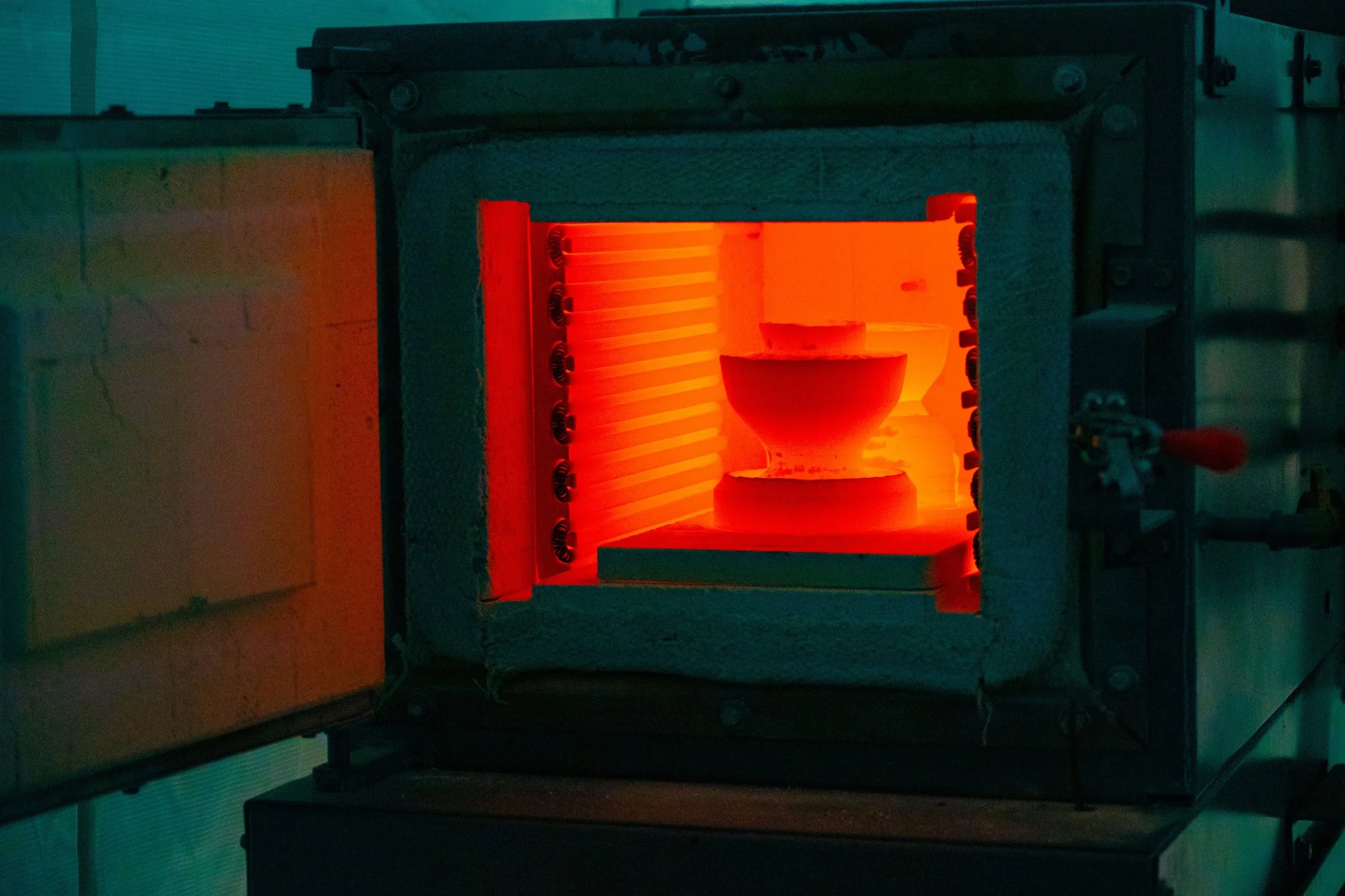 A scientific device or equipment with a glowing orange interior, possibly a 3D printer or an industrial furnace, enclosed within a metallic frame.