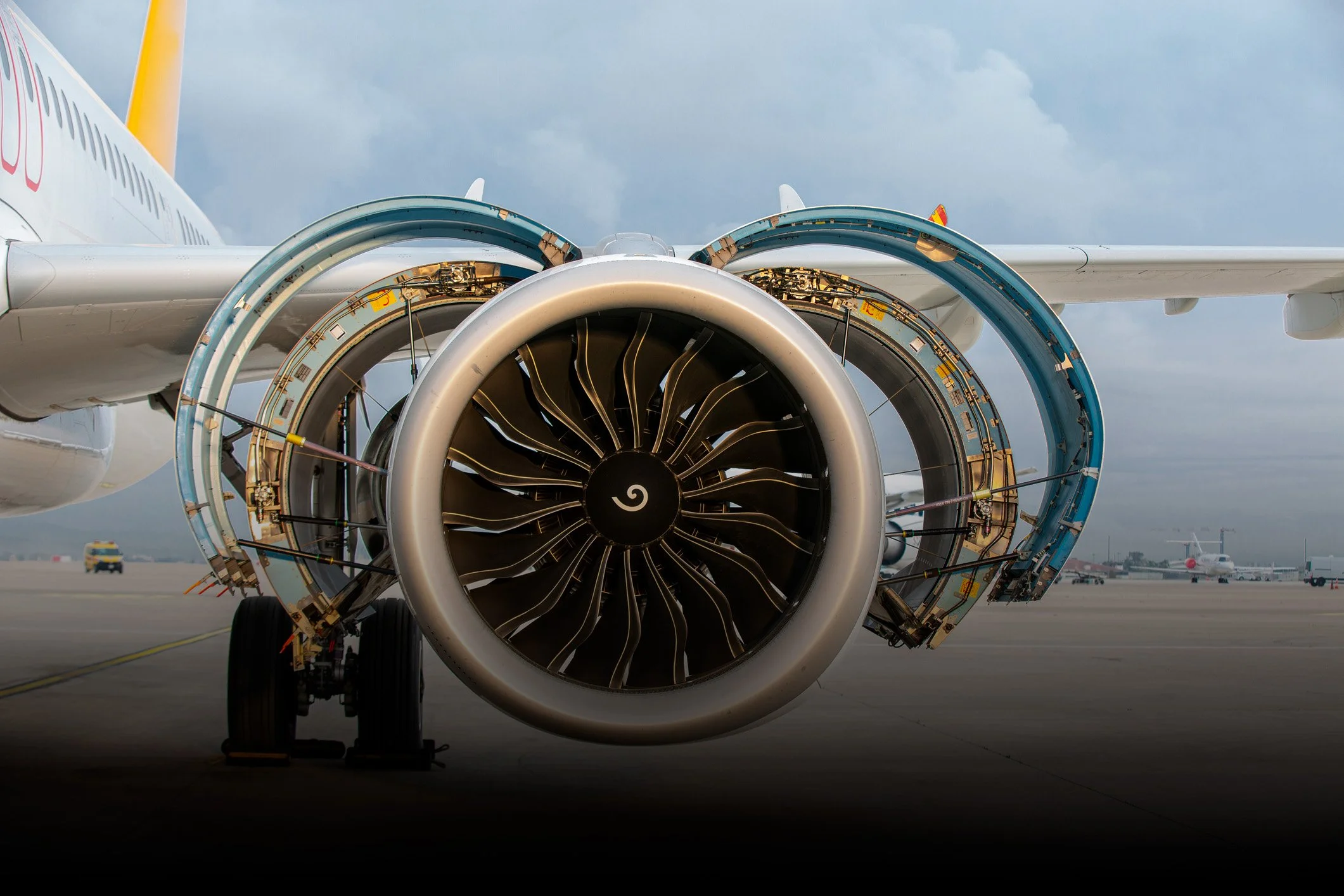 Close-up of a jet engine on an airplane taxiing on the runway, with other airplanes and airport vehicles in the background.