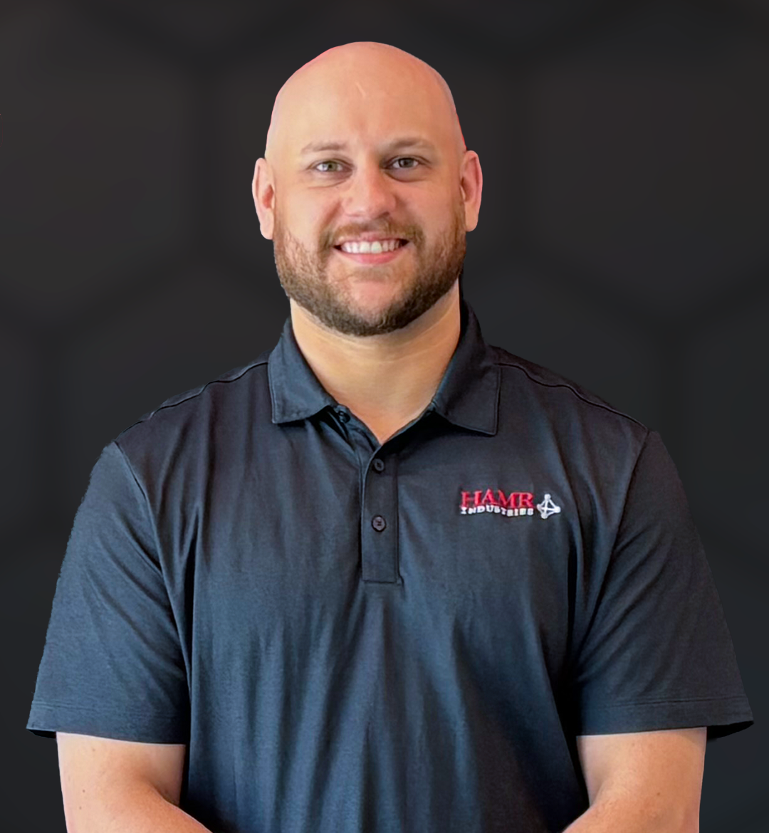 A smiling man with a beard and bald head wearing a black collared shirt with a logo that reads 'HMR Industries'.