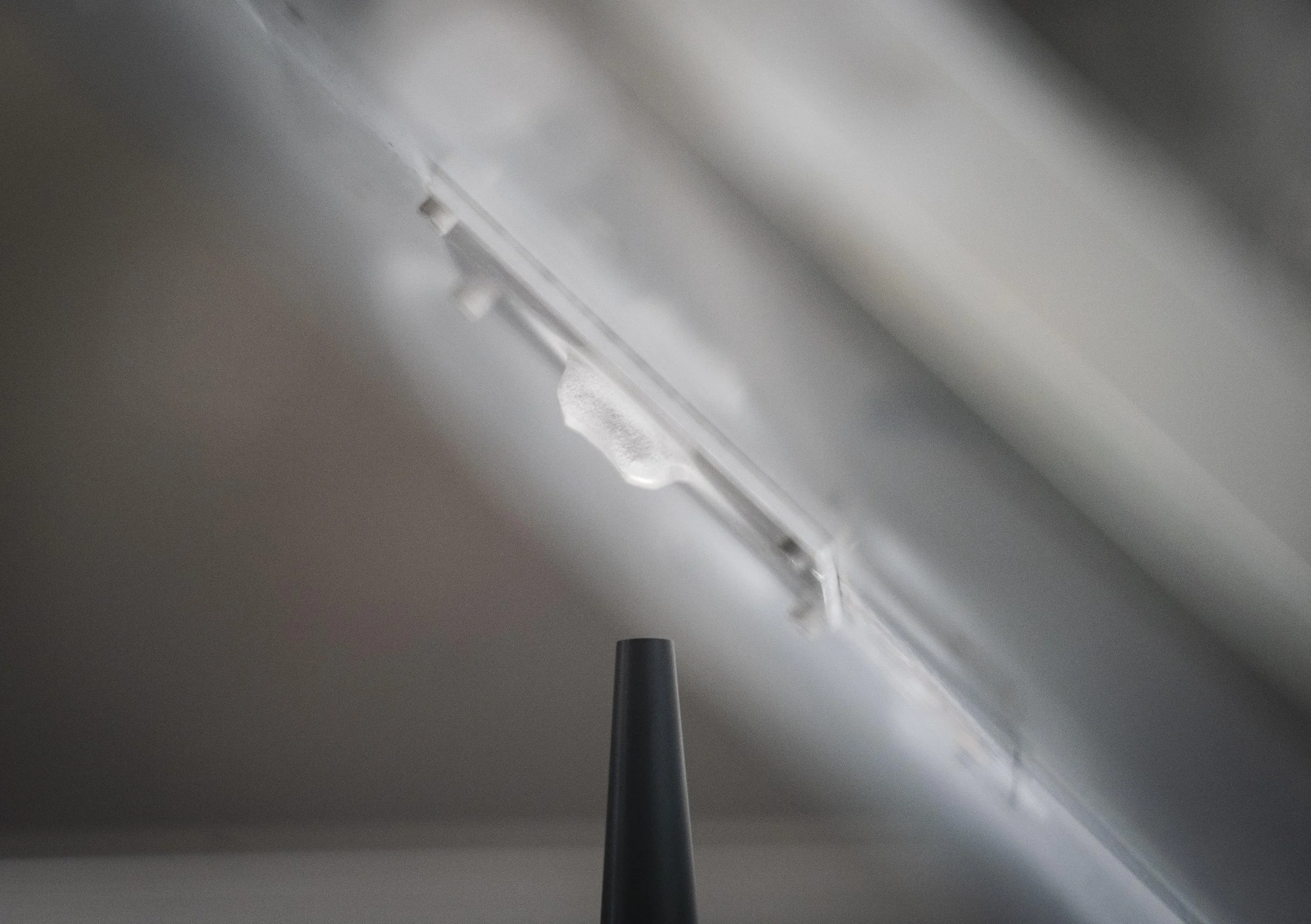 Close-up of a white ceiling with a fluorescent light fixture and a black pole or wire hanging down.