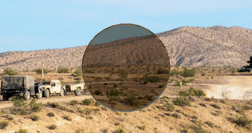 Desert landscape with hills and sparse vegetation, military trucks parked on dirt road.