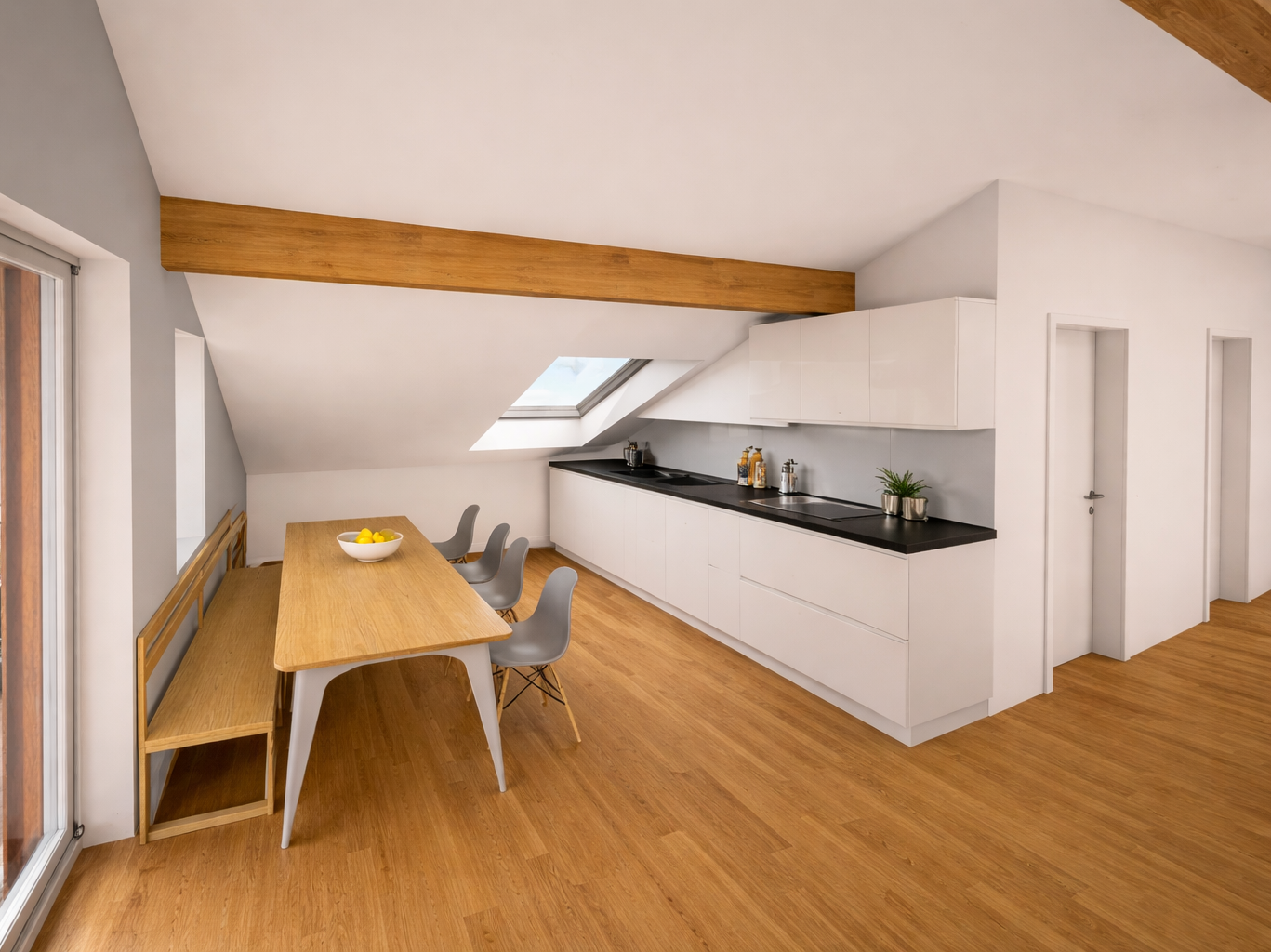 Moderne Küche und Essbereich im Dachgeschoss mit Holzboden, weißen Schränken, schwarzen Arbeitsflächen, Esstisch mit sechs Stühlen und Dachfenster.
