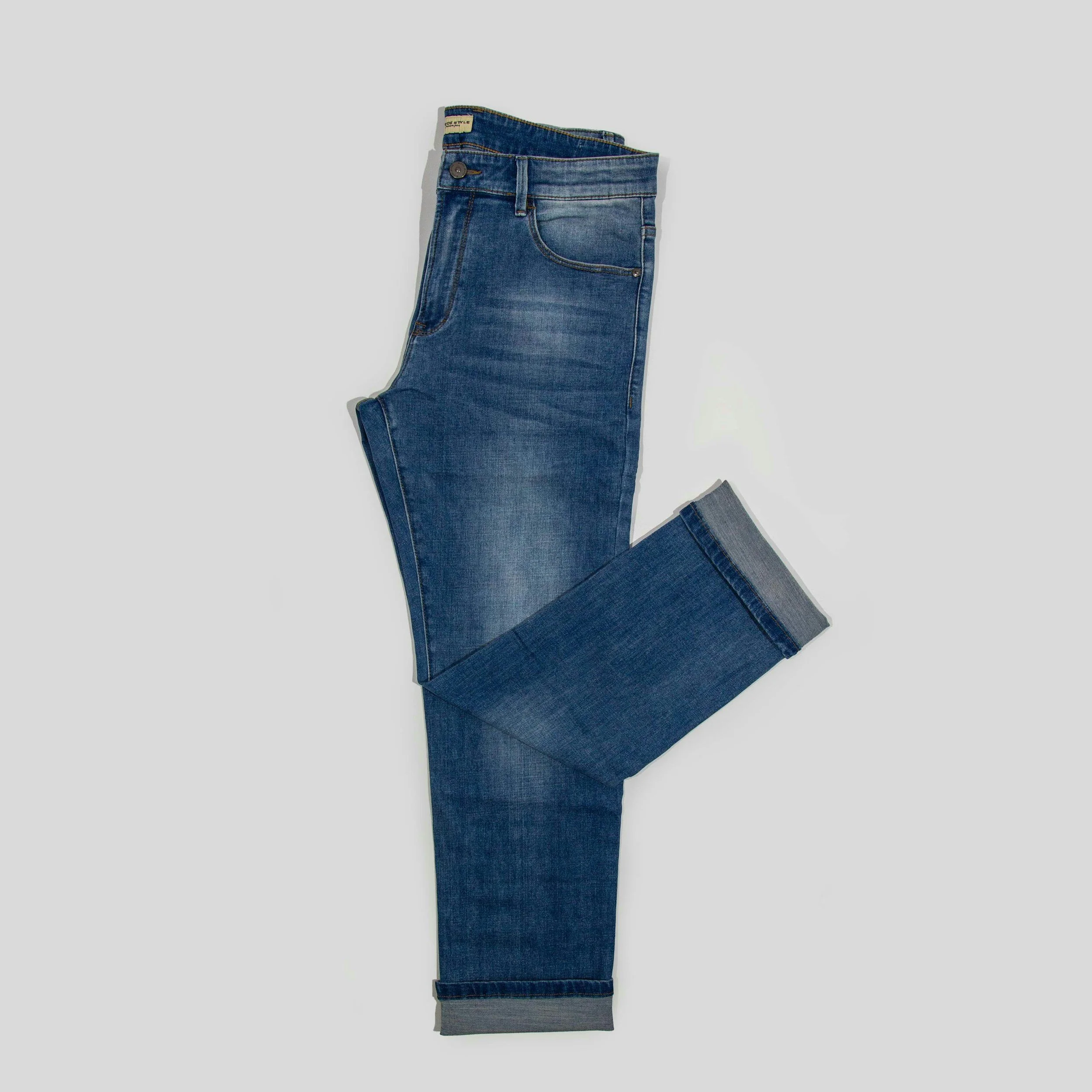 Pair of folded blue jeans with cuffed hems against a gray background.