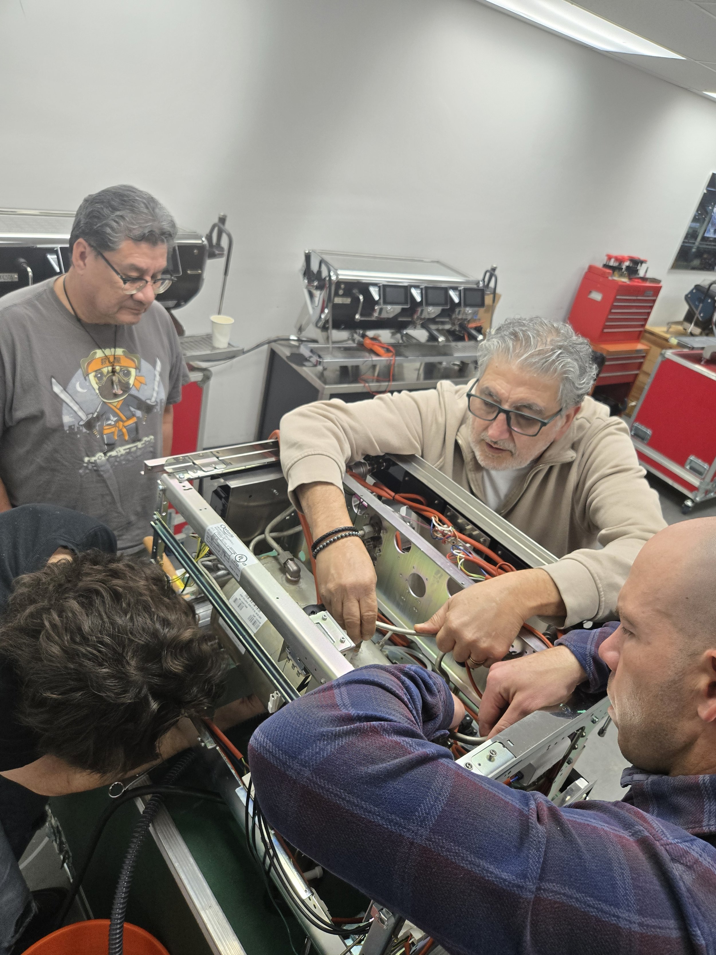 Group of people working together repairing an espresso machine in a workshop.