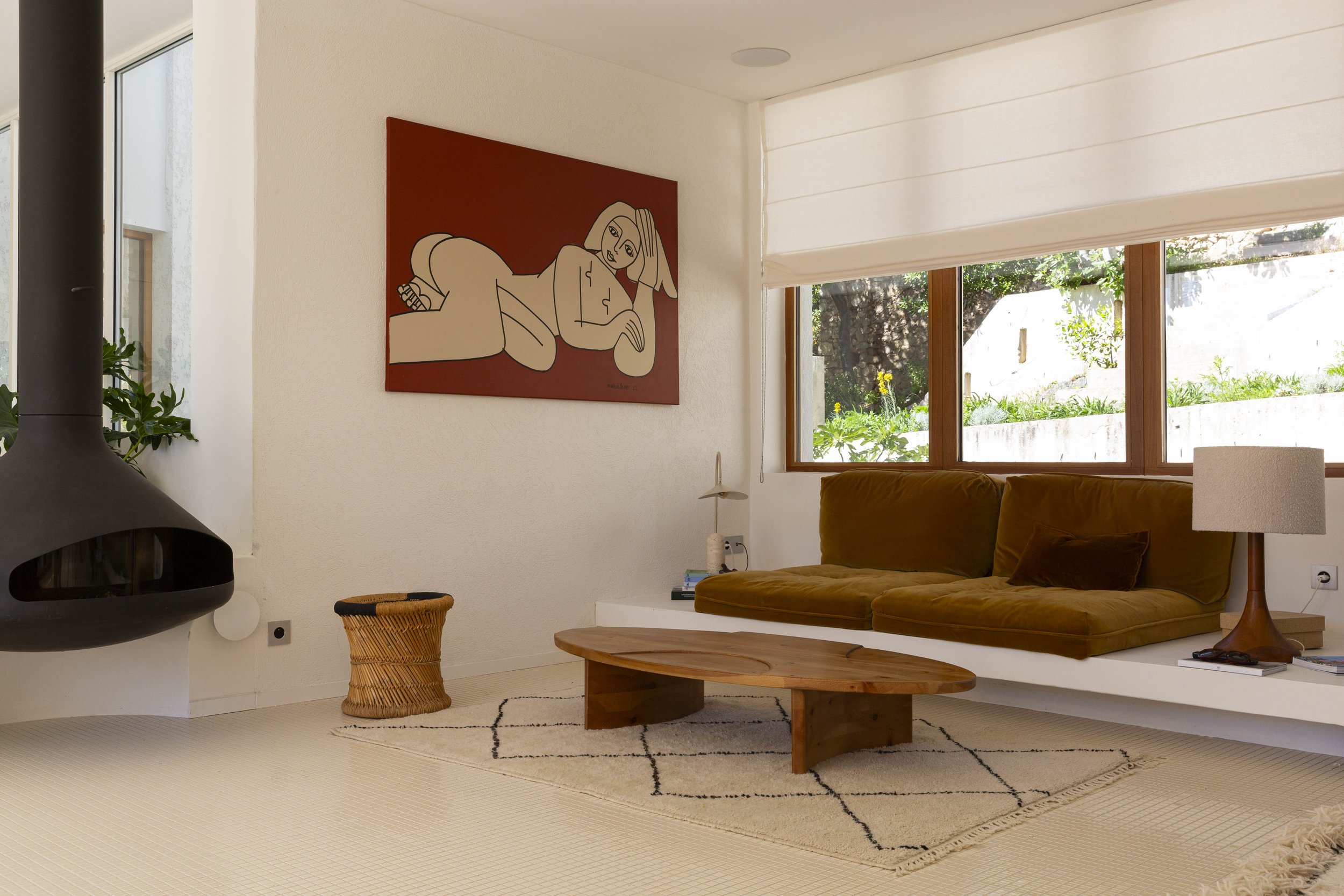Salon moderne avec un canapé en velours beige, une table en bois, une œuvre d'art abstraite sur le mur, une grande fenêtre laissant entrer la lumière naturelle, un tapis beige clair et une cheminée.