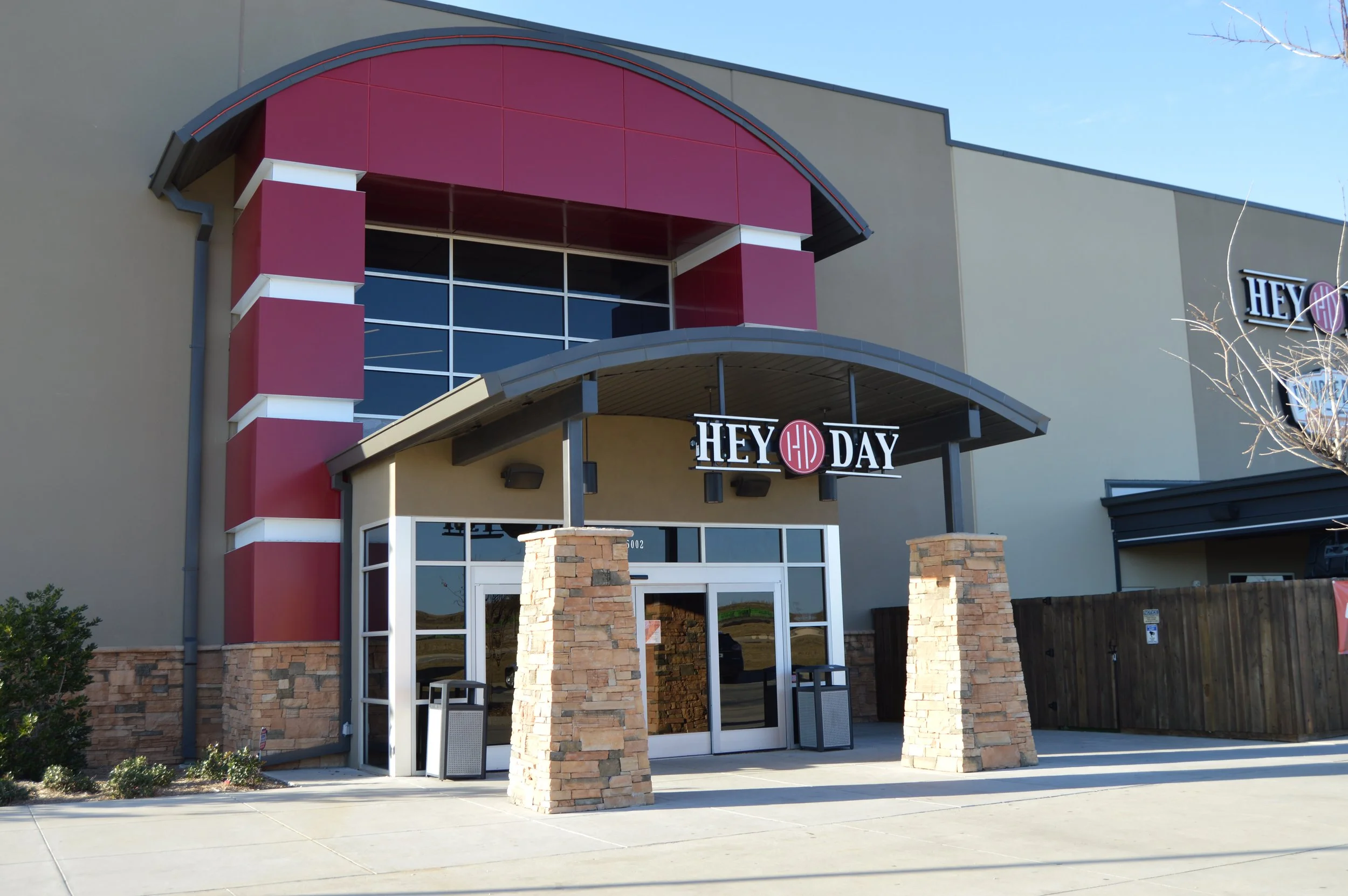 Exterior of a shopping mall with a sign for Heyday, a skincare store, featuring stone columns and large glass windows.