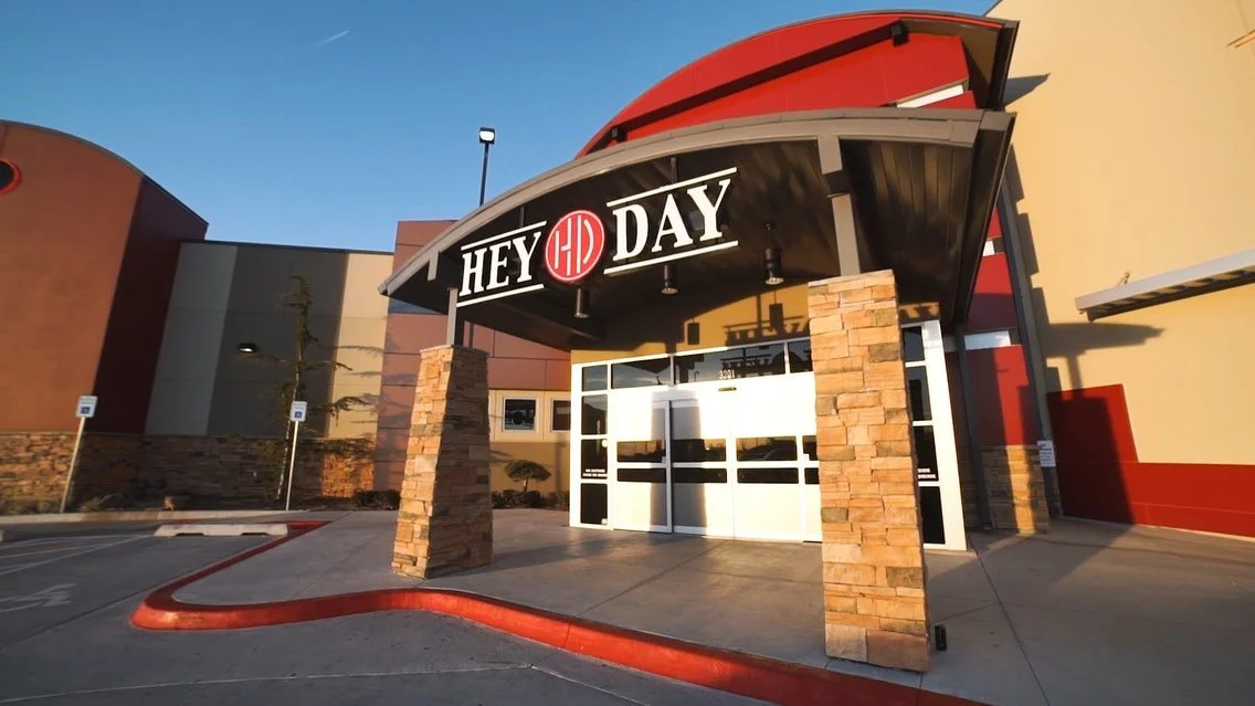 The entrance to a Hey Day restaurant or entertainment venue with a curved awning, brick columns, and a sign with red and white branding.
