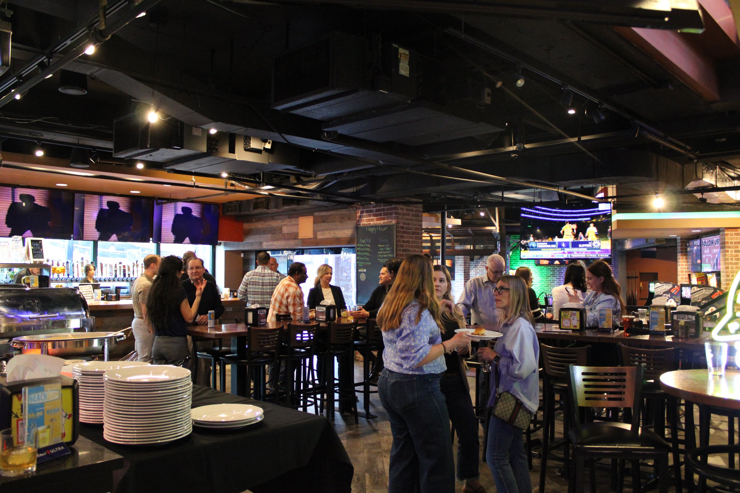 People socializing and having drinks at a bar or pub with multiple TVs showing a sporting event