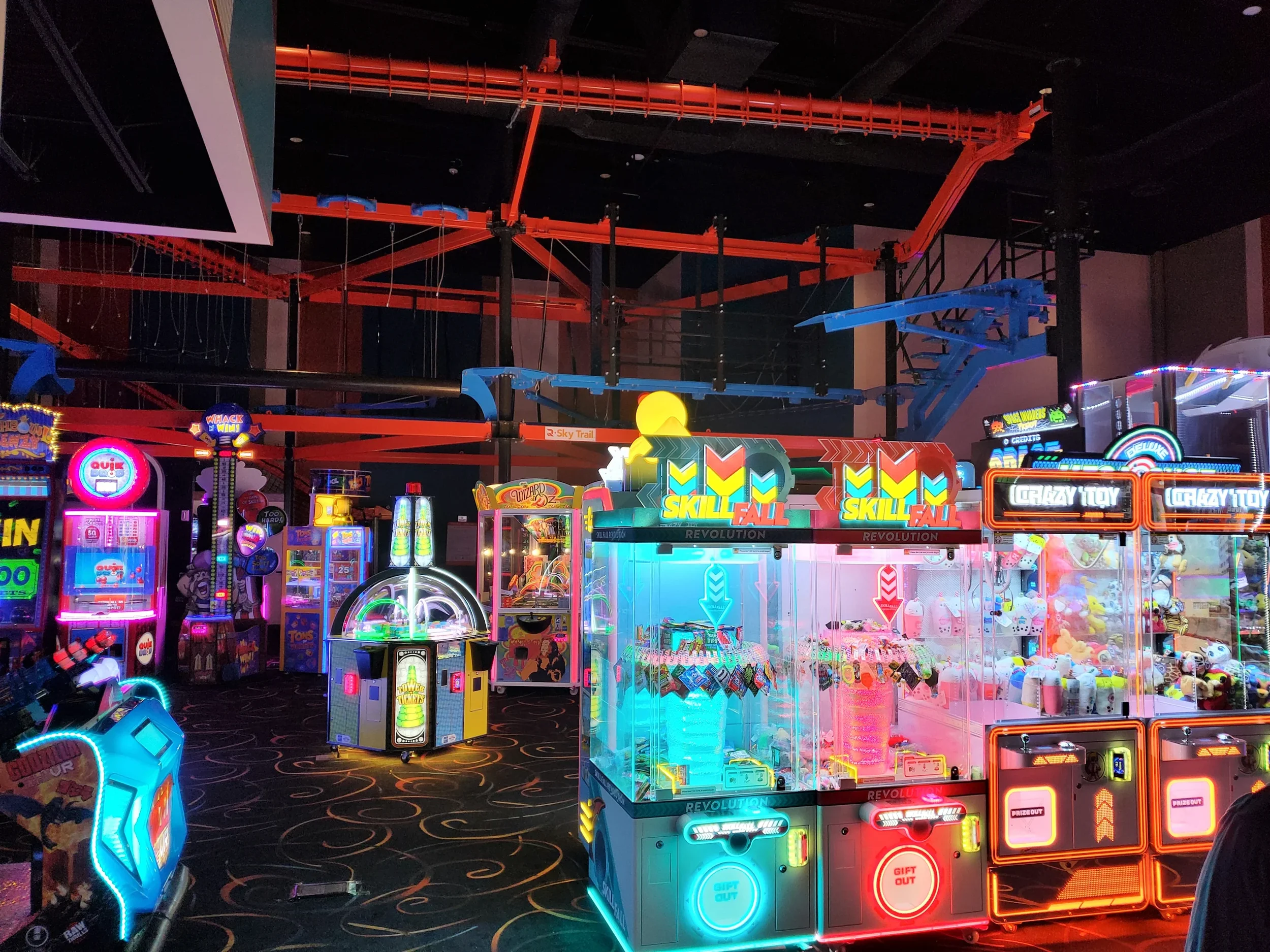 Colorful arcade game machines and prize claw machines in an amusement center, illuminated with bright neon lights.