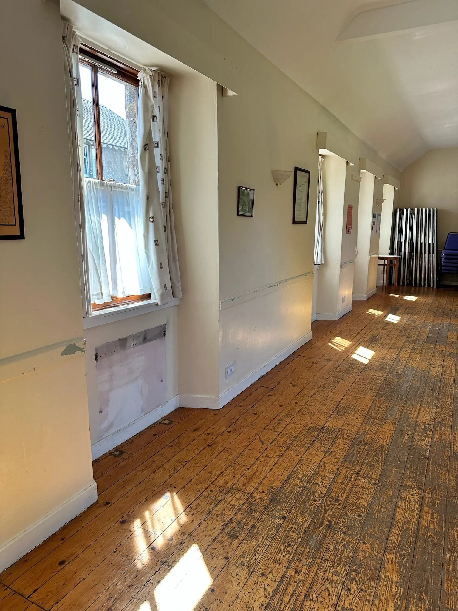 Sunlight streaming through multiple windows with white curtains illuminating a wooden floor in a room.