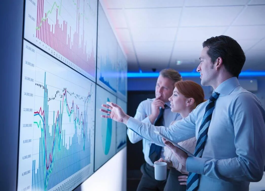 Three business professionals analyzing data and graphs on large screens in a modern office.