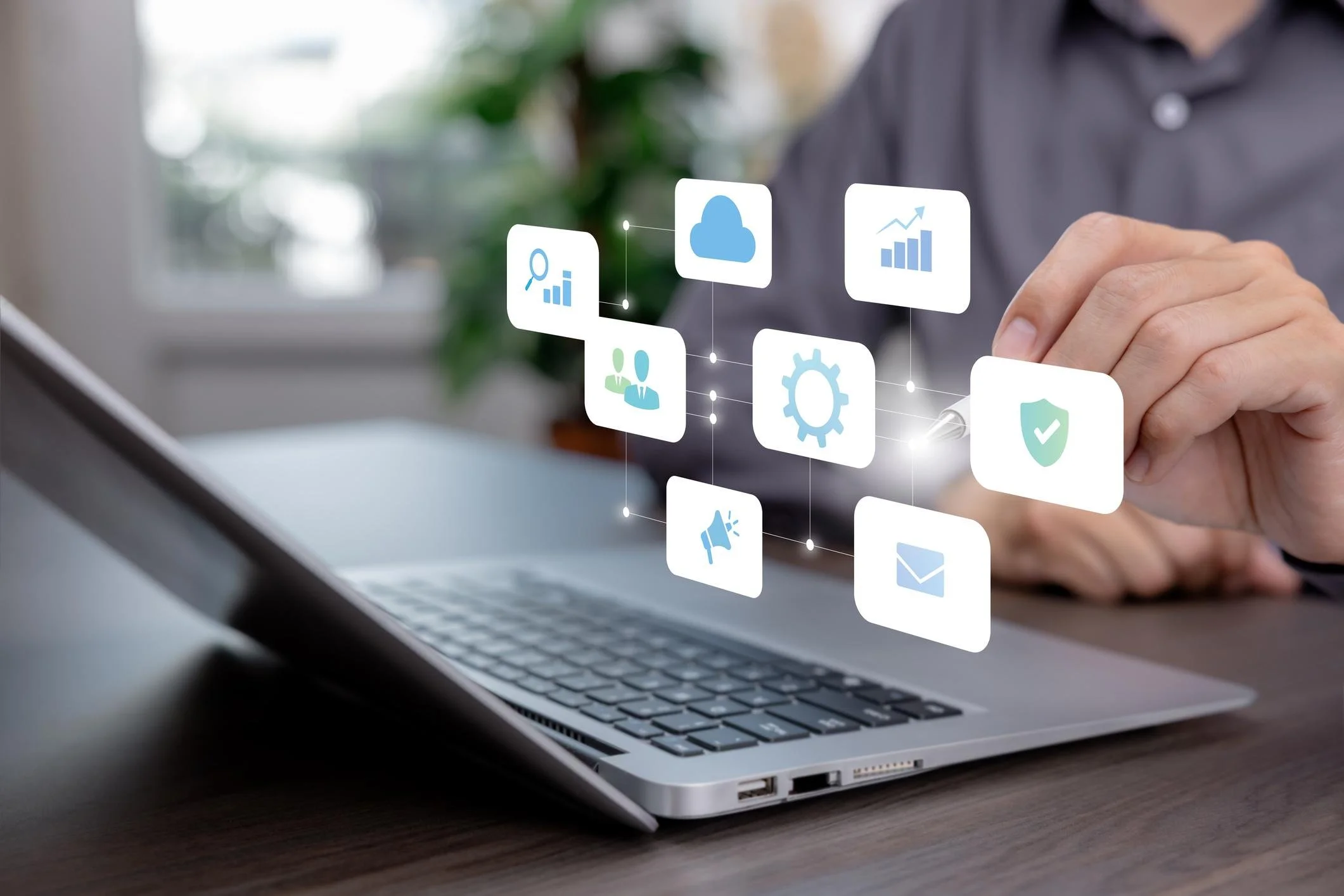 A person using a laptop with a virtual interface displaying various digital icons and graphs, including a magnifying glass, cloud, upward graph, gear, shield, megaphone, and email, suggestive of technology or digital tools.
