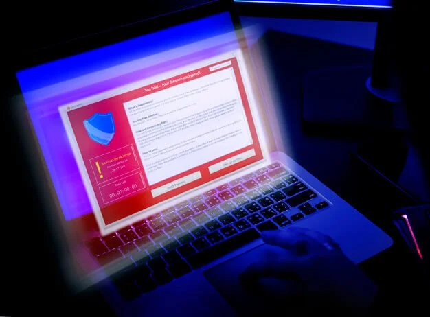 A person using a laptop computer with a red warning alert on the screen, displaying a security shield icon and a message about a security threat.