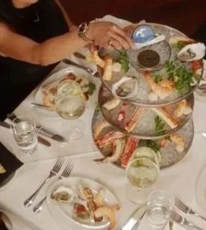 A person reaching for food on a tiered serving tray at a dining table with plates, glasses, and utensils.
